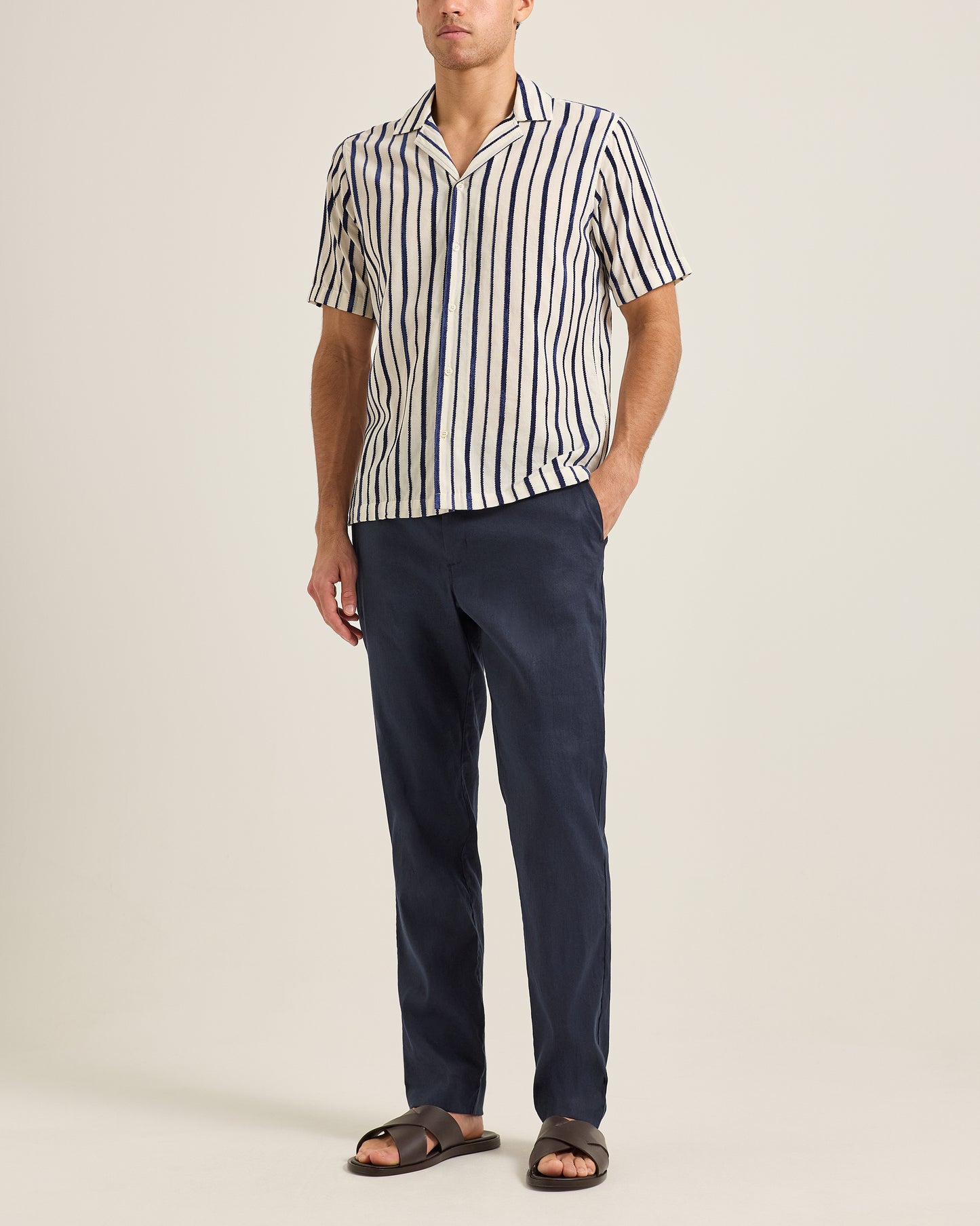 Man wearing a striped shirt and navy pants on a plain background