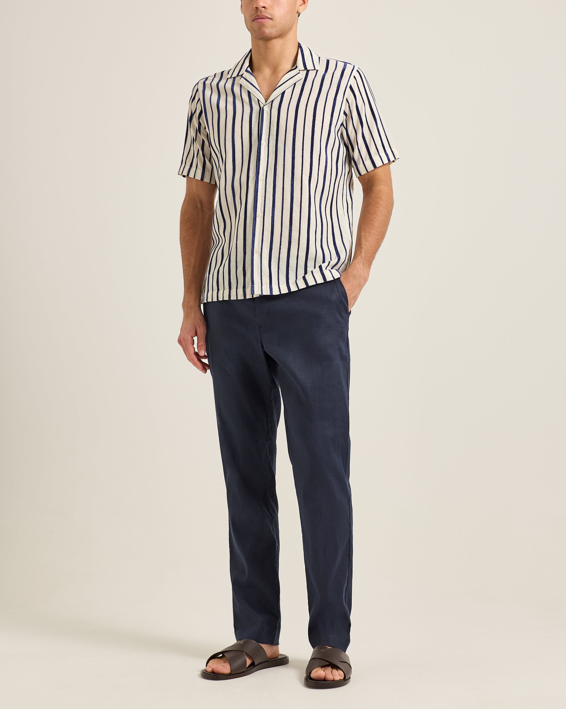 Man wearing a striped shirt and navy pants on a plain background