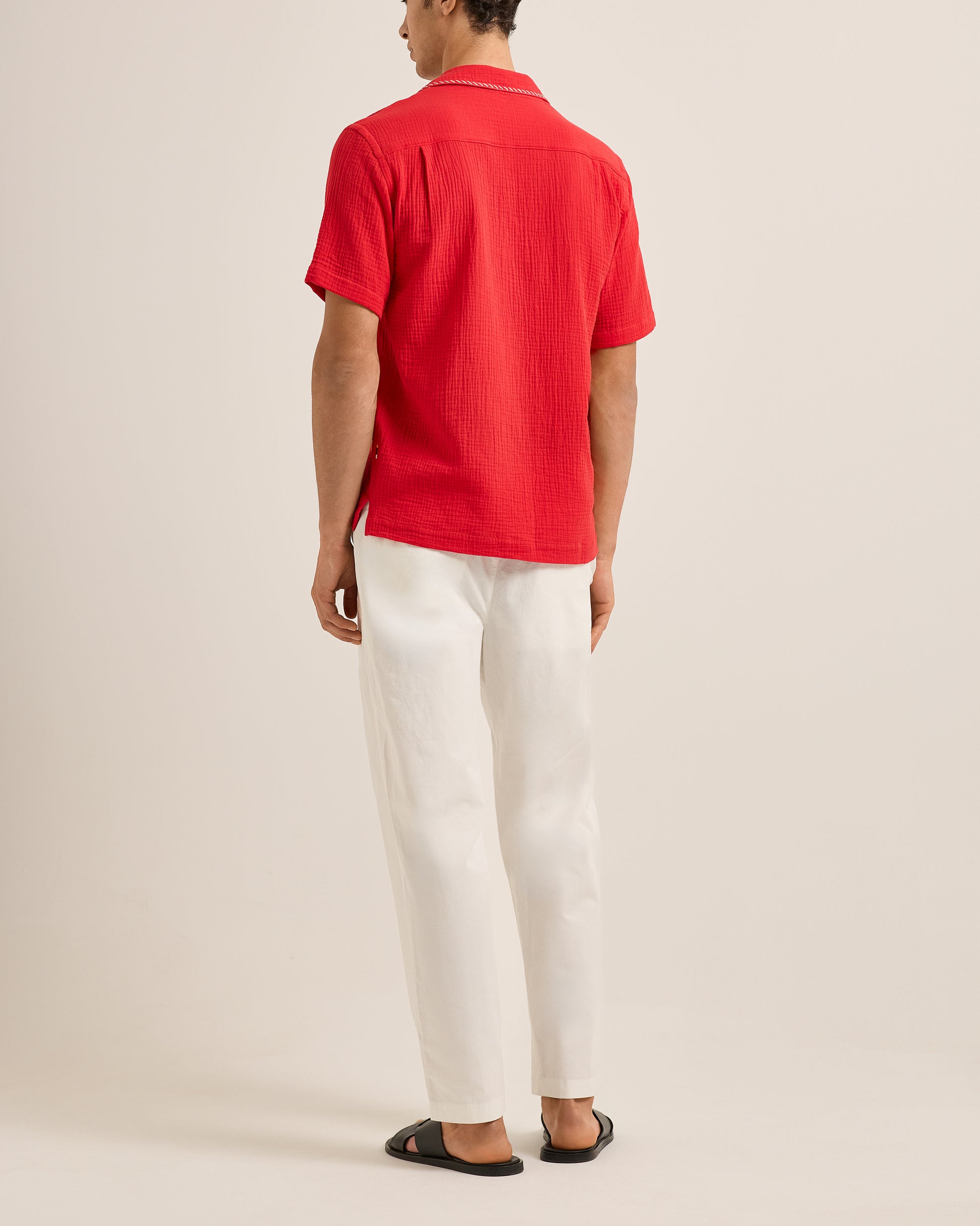 Person wearing a red shirt and white pants on a plain background