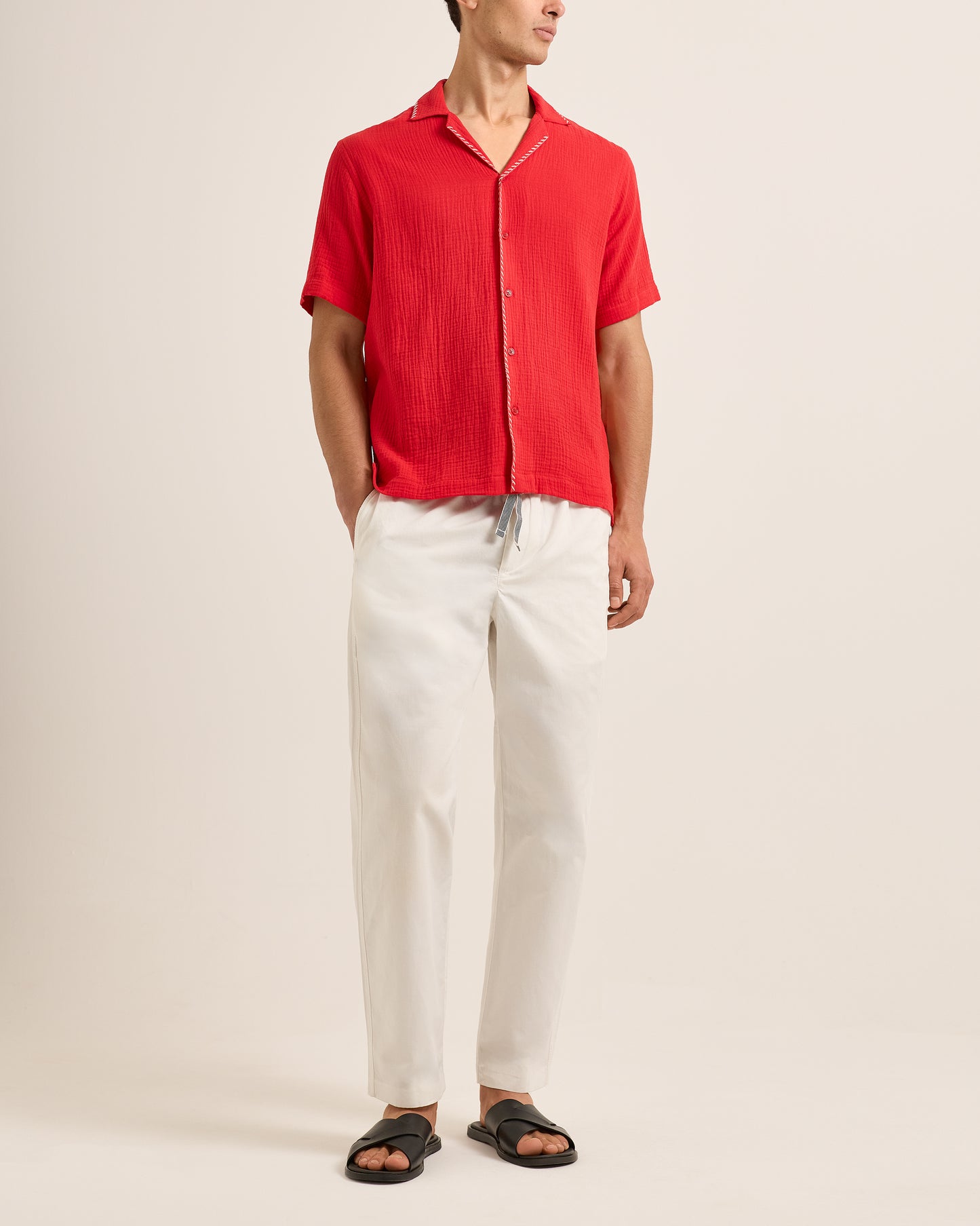 Person wearing a red short-sleeve shirt and white pants on a beige background