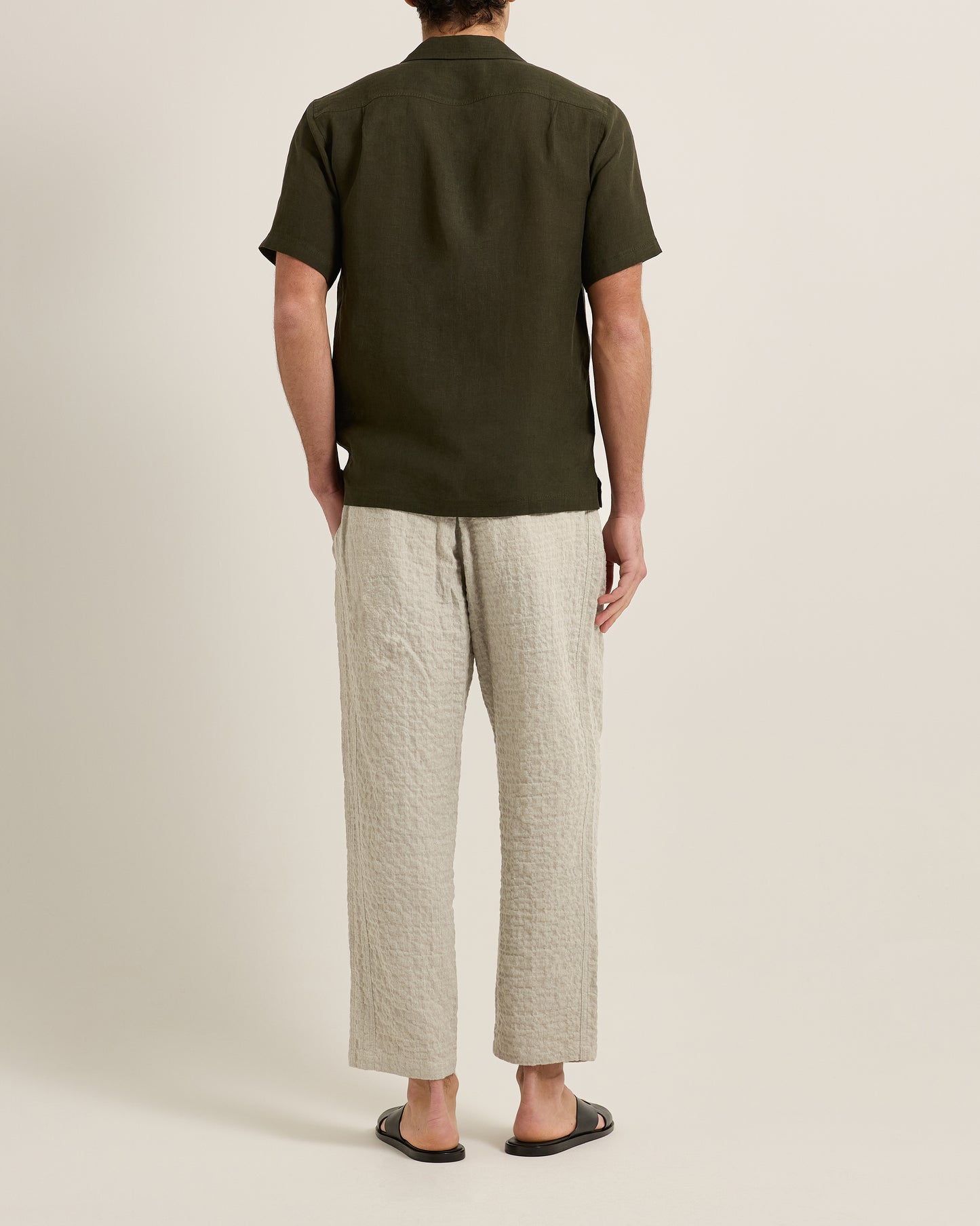 Person wearing a green polo shirt and beige pants on a plain background