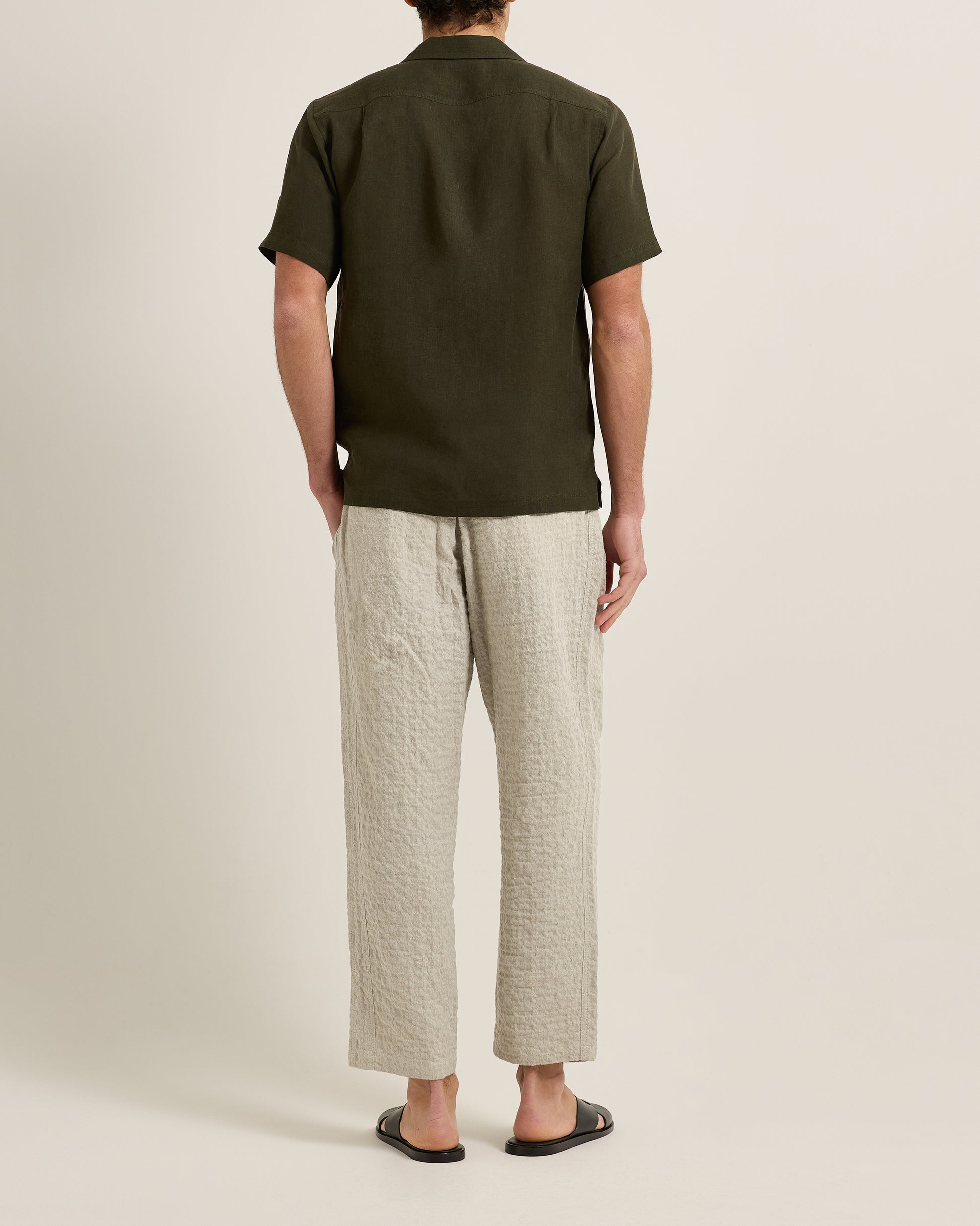 Person wearing a green polo shirt and beige pants on a plain background