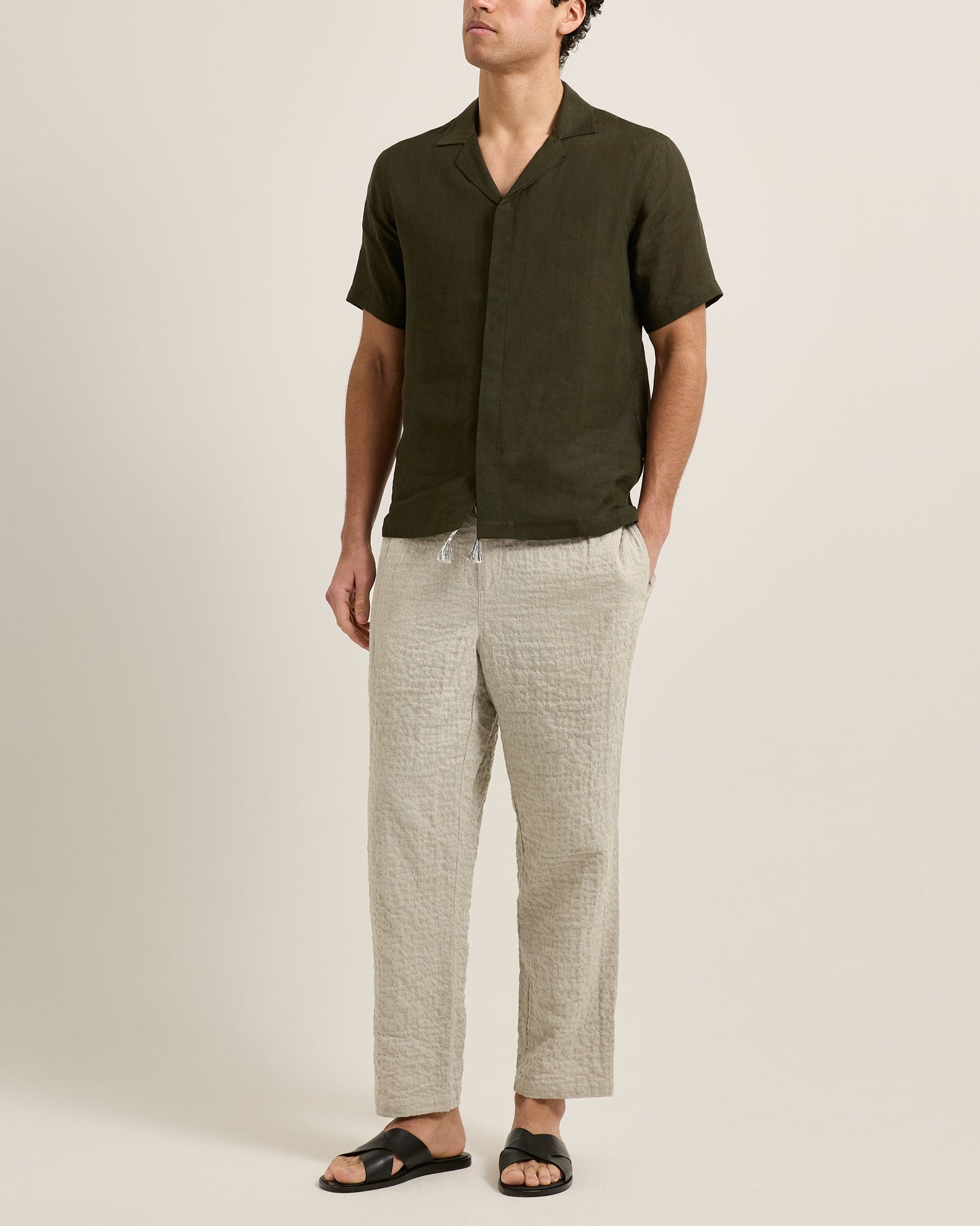 Man wearing a dark green shirt and light gray pants on a beige background