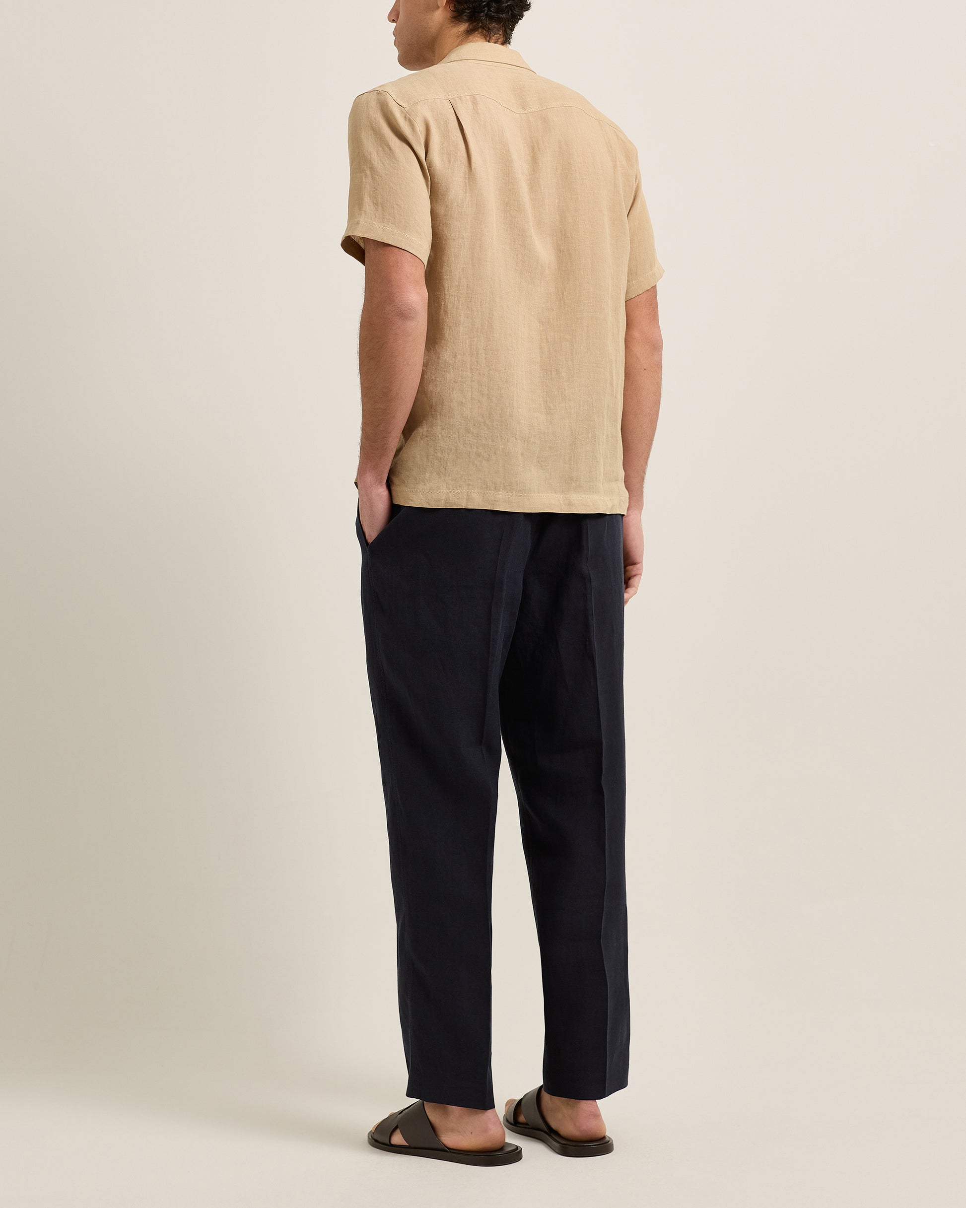 Person wearing a beige shirt and black pants on a plain background