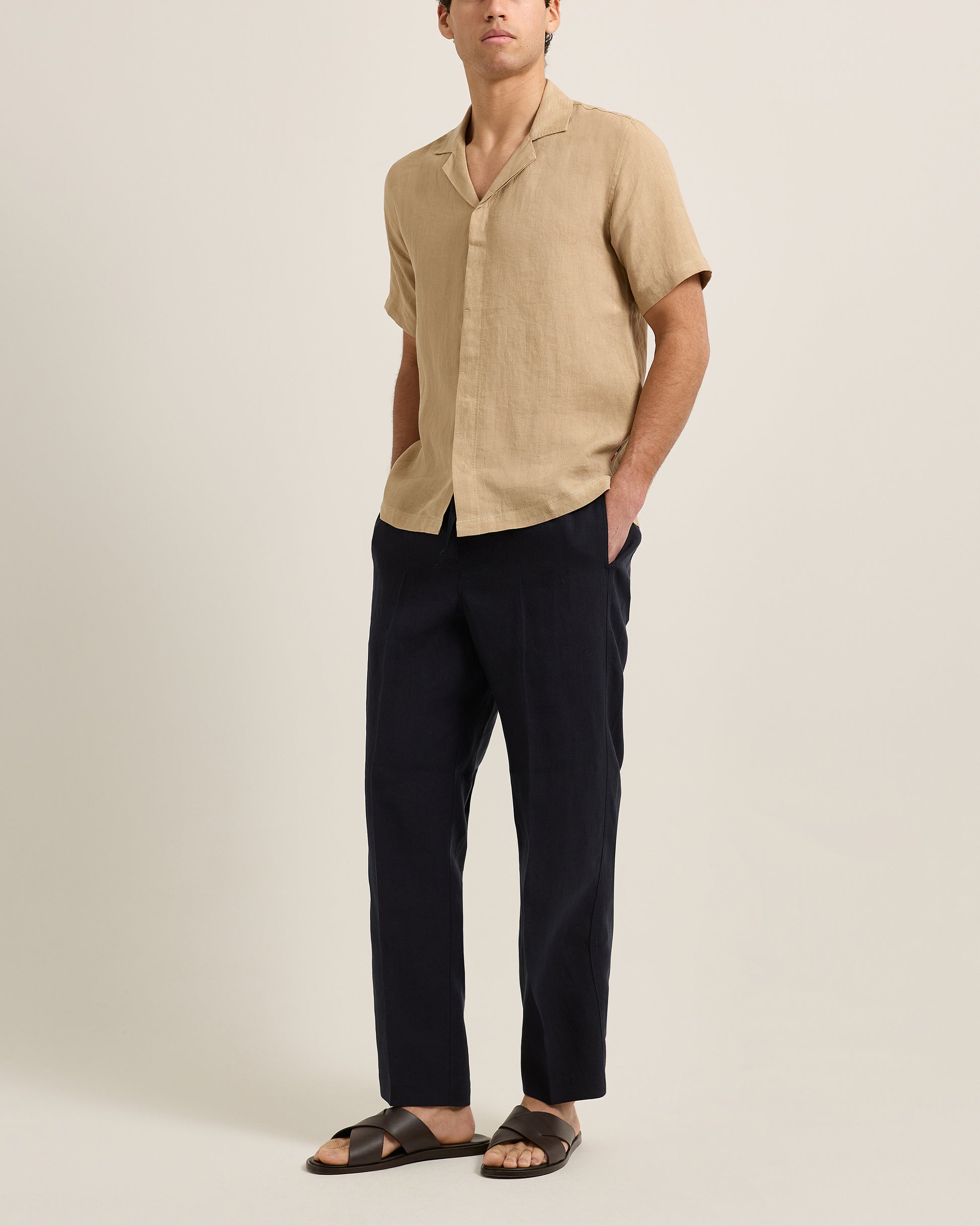 Man wearing a beige shirt and dark pants on a plain background