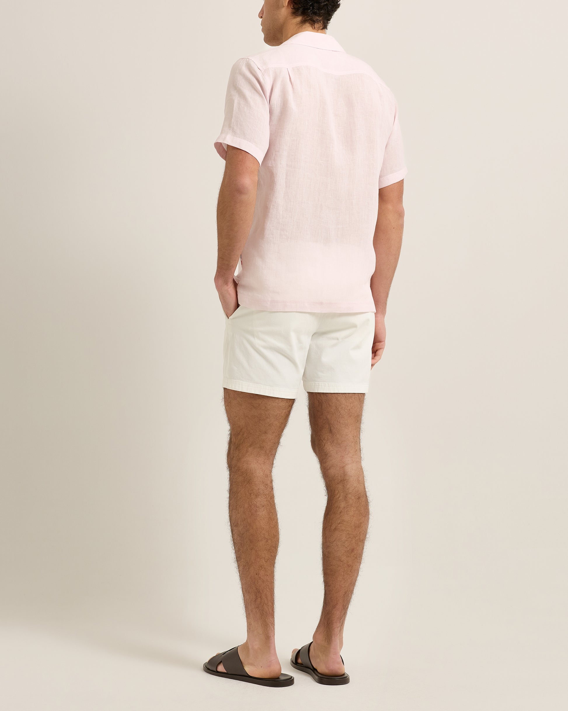 Man wearing a light pink polo shirt and white shorts on a plain background