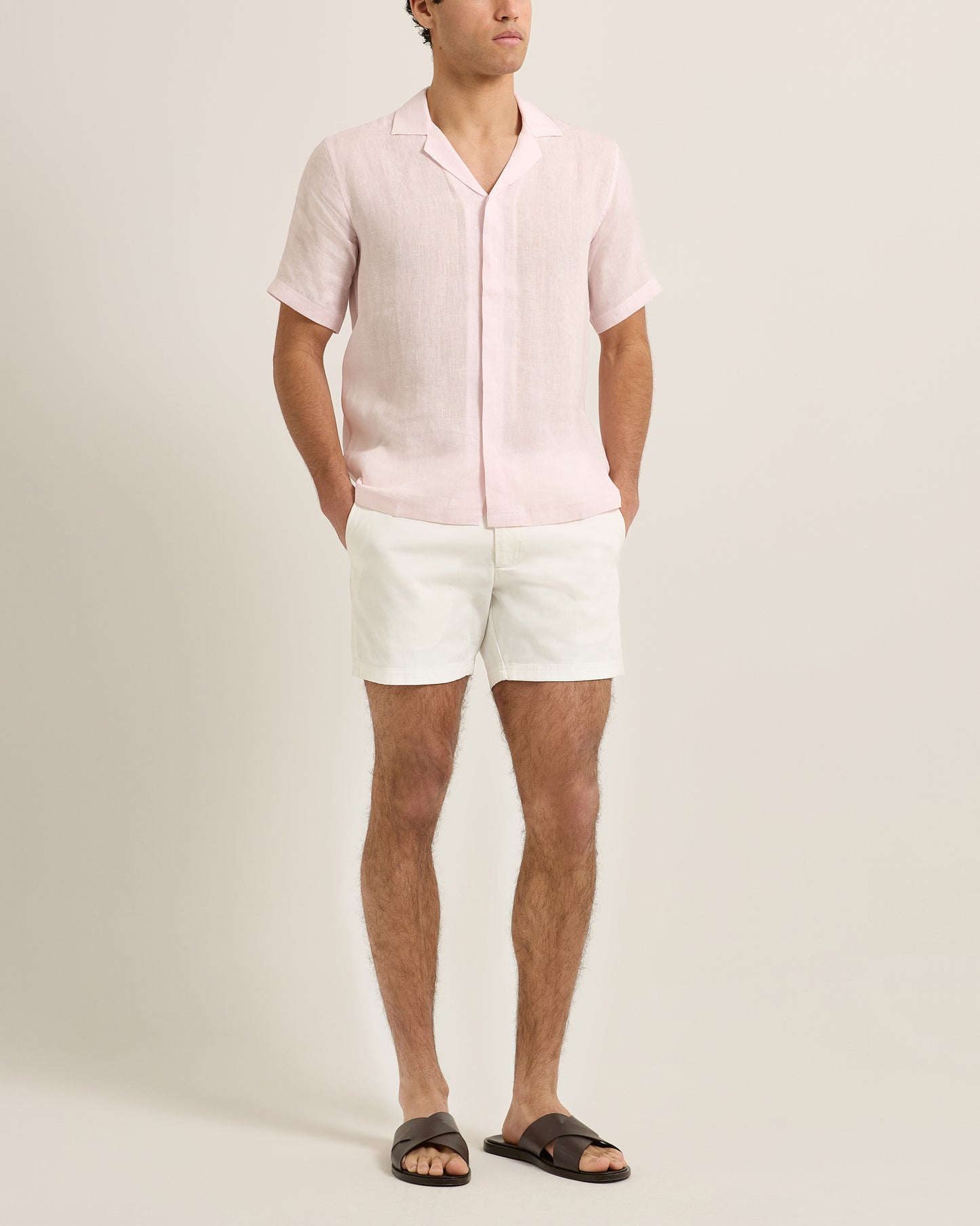 Person wearing a light pink linen shirt and white shorts on a plain background
