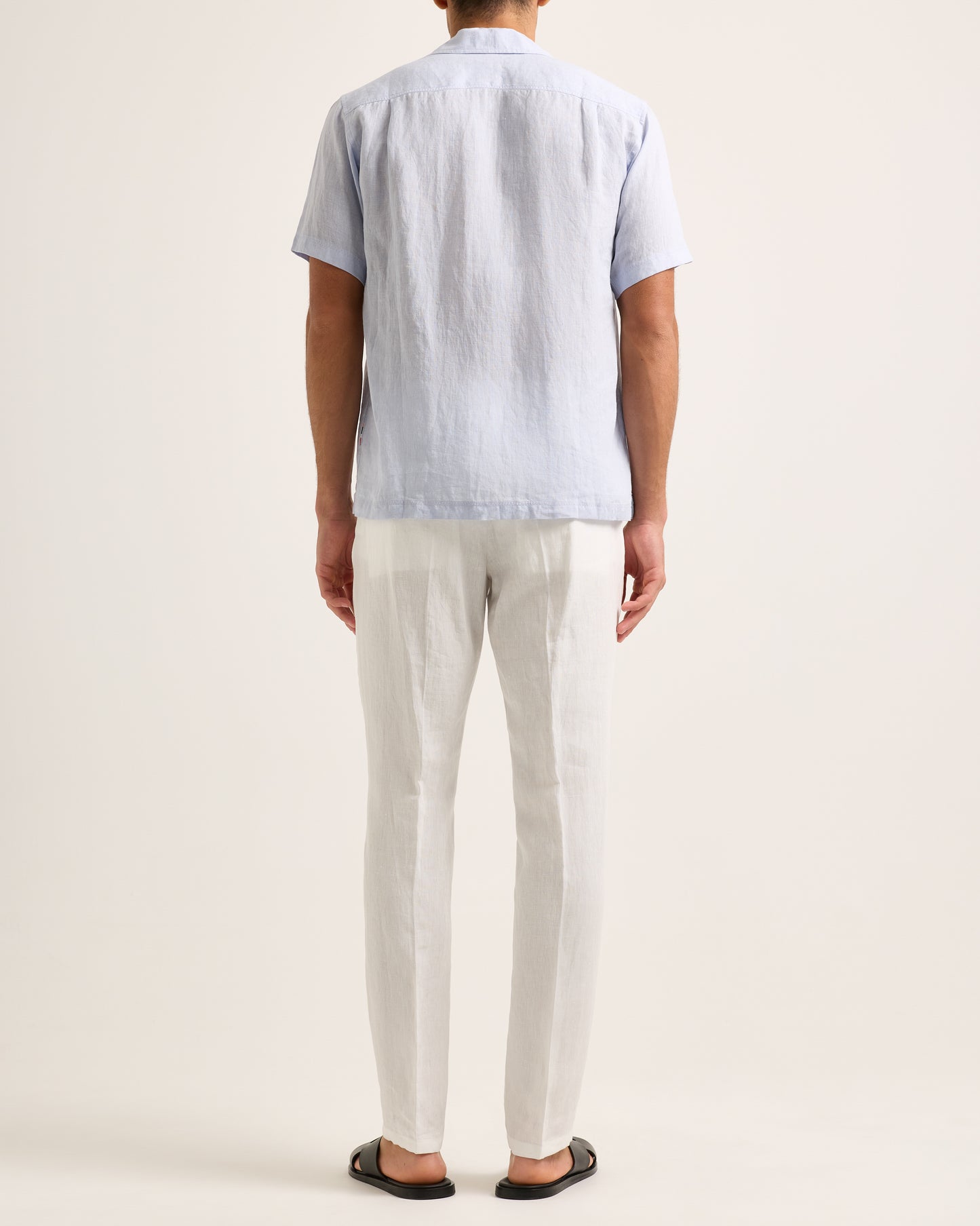 Model wearing light blue short-sleeve shirt with white trousers on a white background