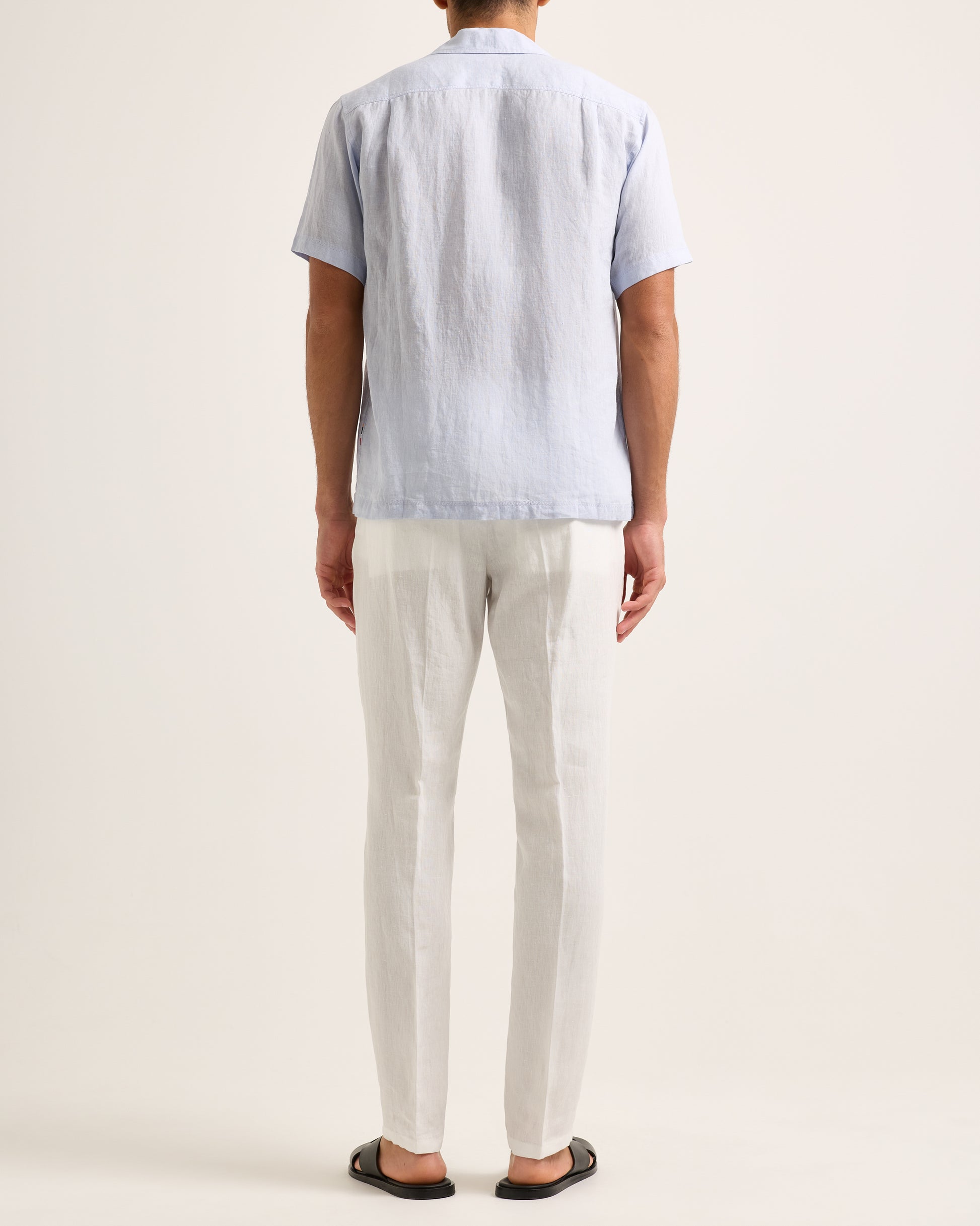 Model wearing light blue short-sleeve shirt with white trousers on a white background