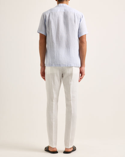 Model wearing light blue short-sleeve shirt with white trousers on a white background