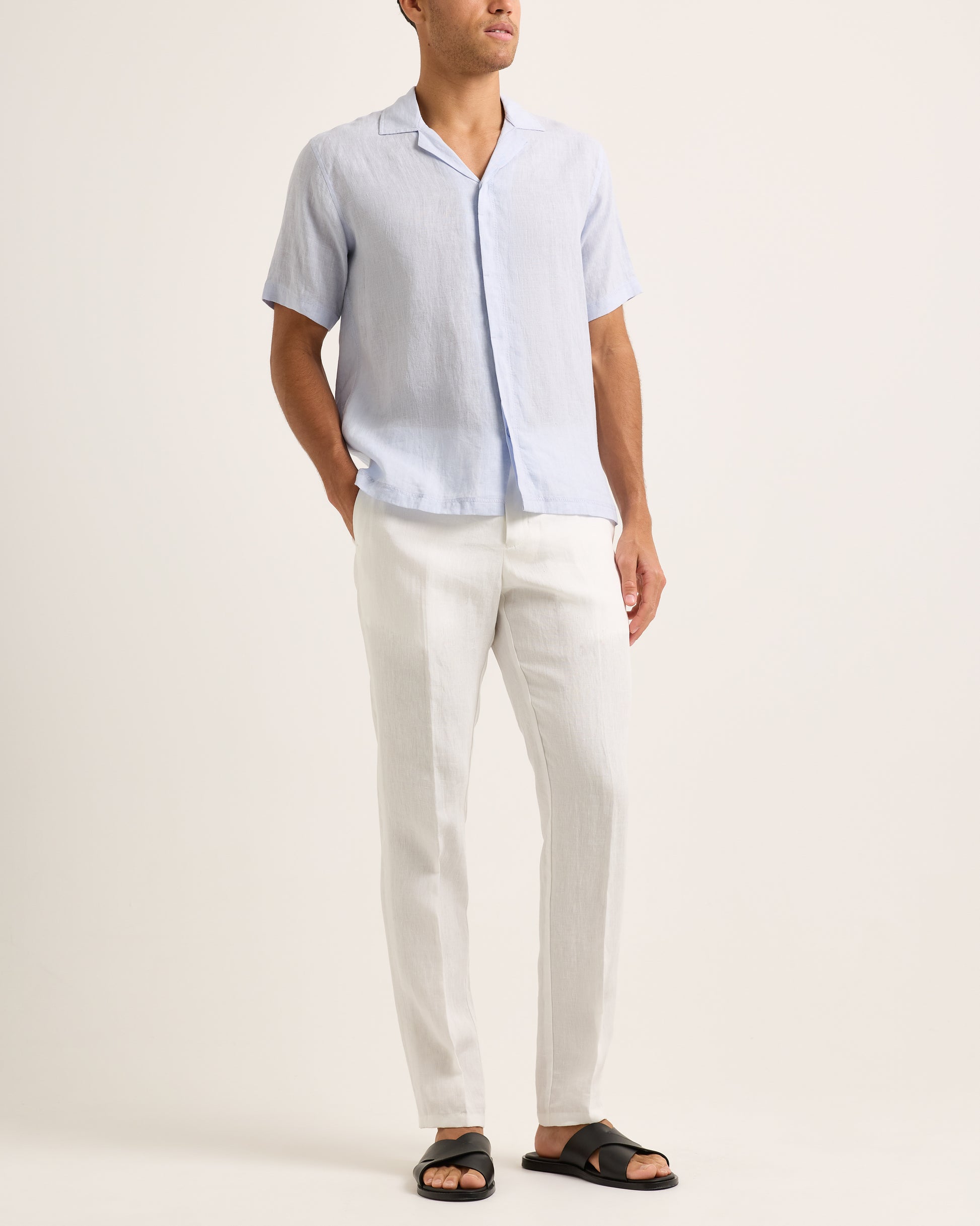 Model wearing light blue short-sleeve shirt with white trousers on a white background