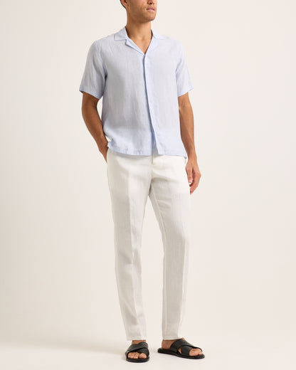 Model wearing light blue short-sleeve shirt with white trousers on a white background