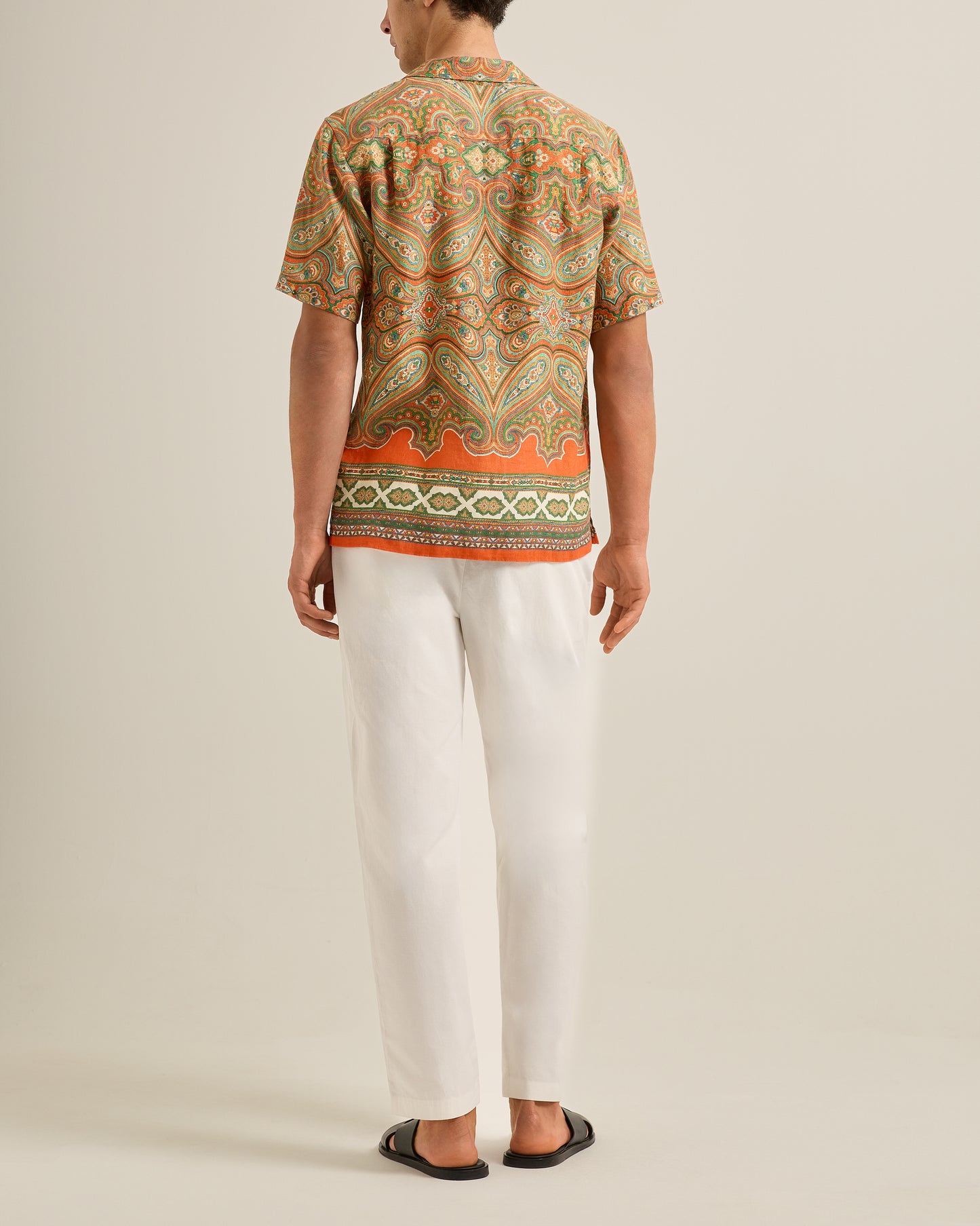 Person wearing a patterned shirt and white pants on a plain background