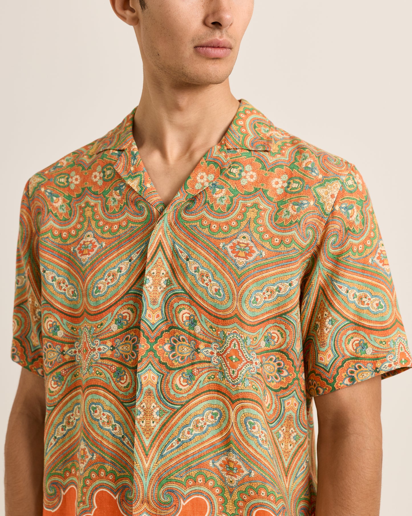 Man wearing a patterned shirt with orange and green colors on a beige background