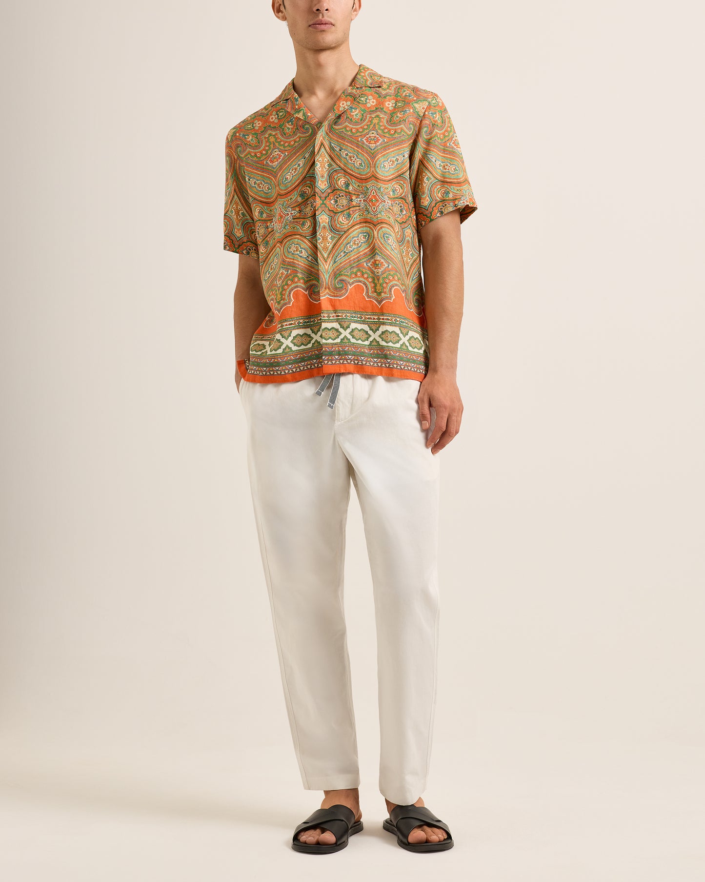 Person wearing a patterned shirt and white pants on a plain background