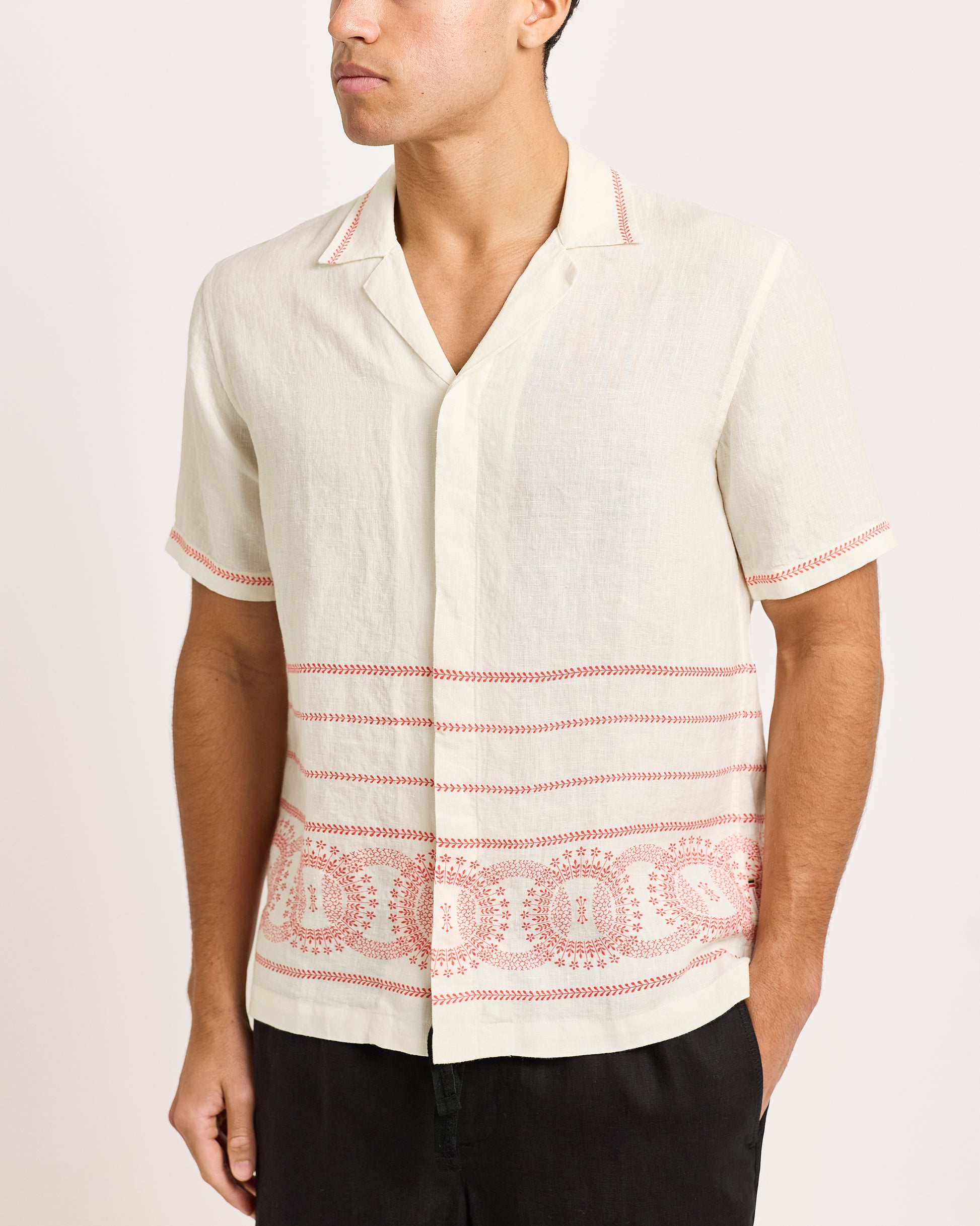 Man wearing a white short-sleeve shirt with red patterns on a plain background