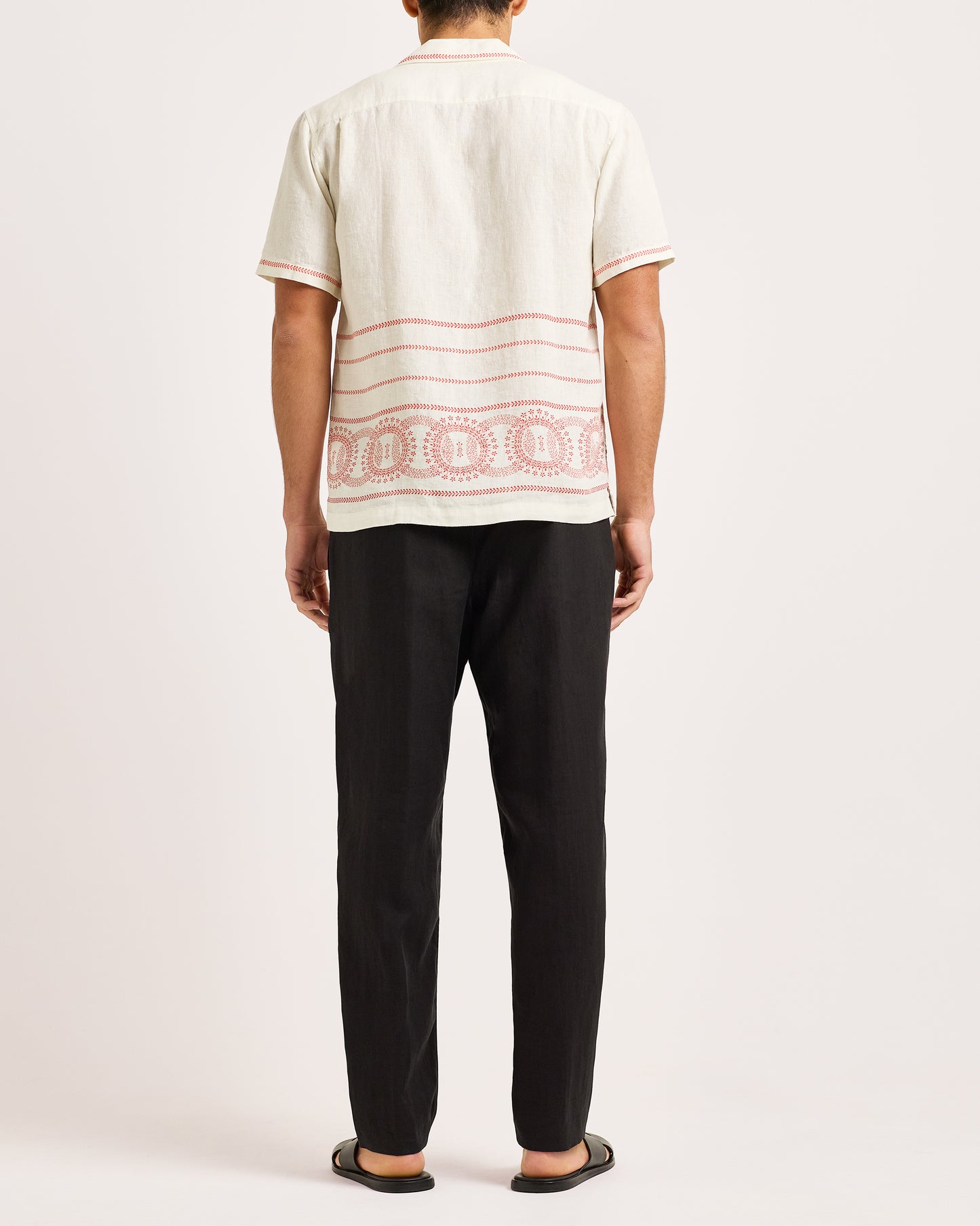 Person wearing a white shirt with red patterns and black pants on a white background