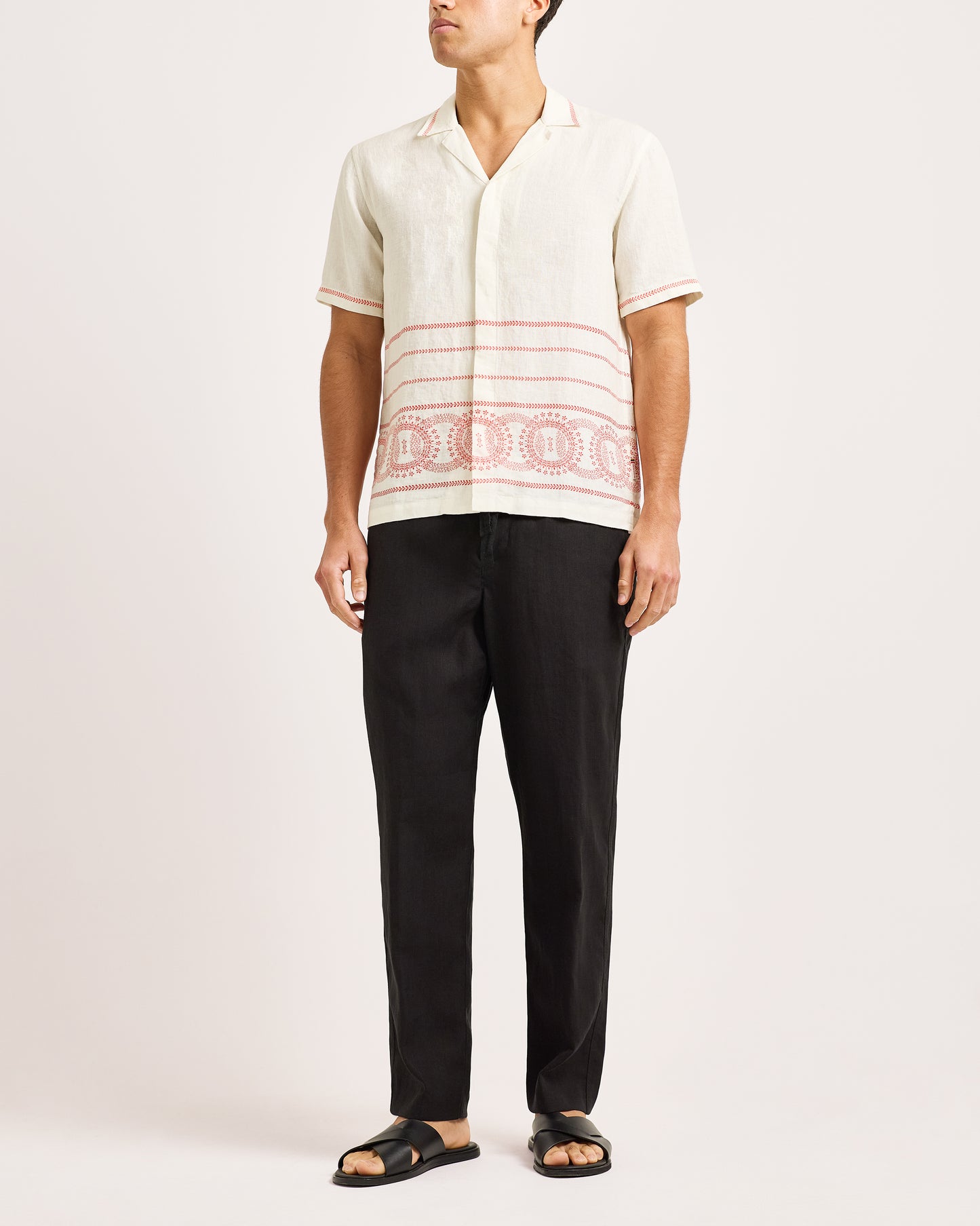 Person wearing a white shirt with red patterns and black pants on a white background