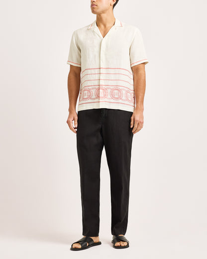 Person wearing a white shirt with red patterns and black pants on a white background