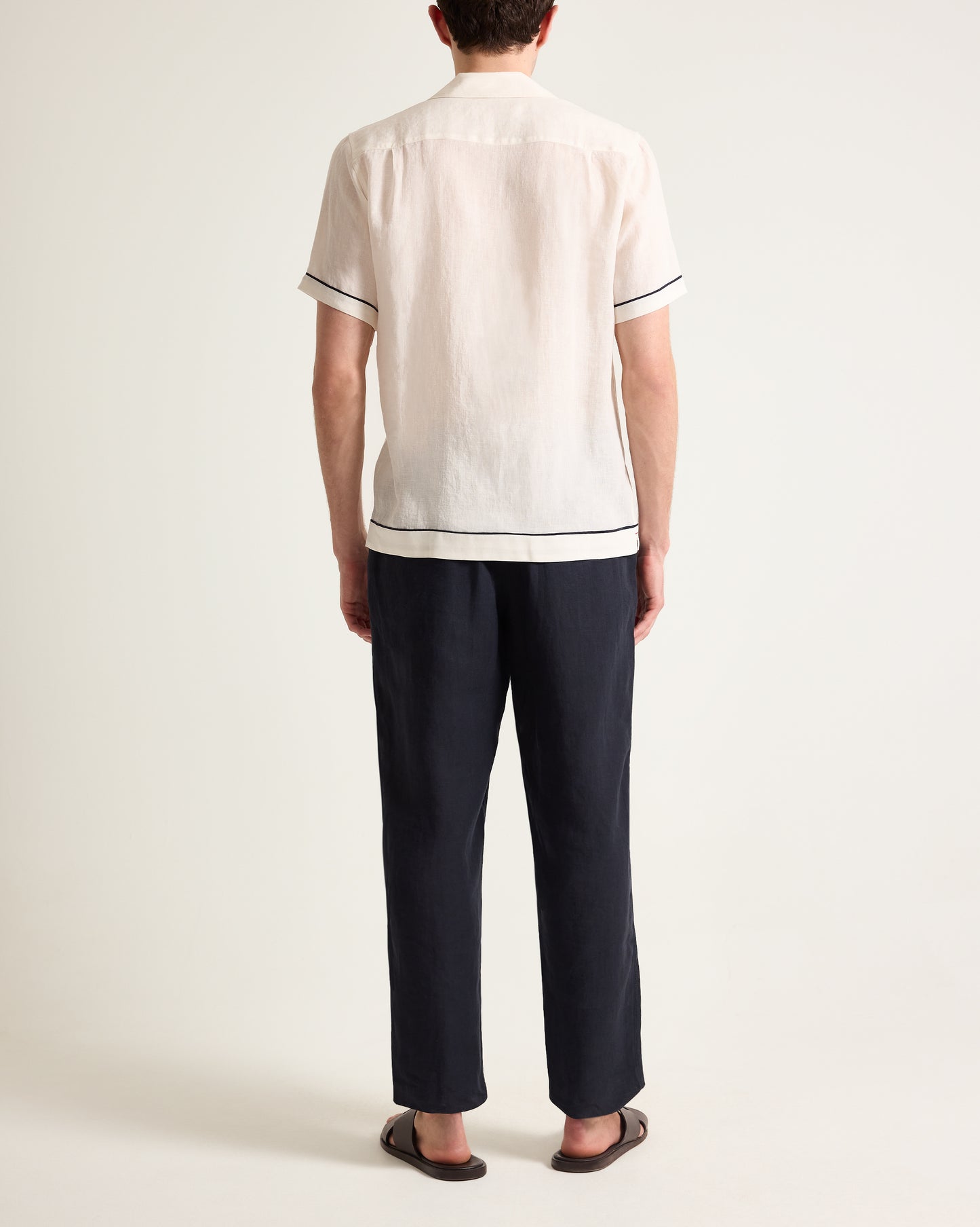 Person wearing a white shirt with black trim and dark pants on a plain background