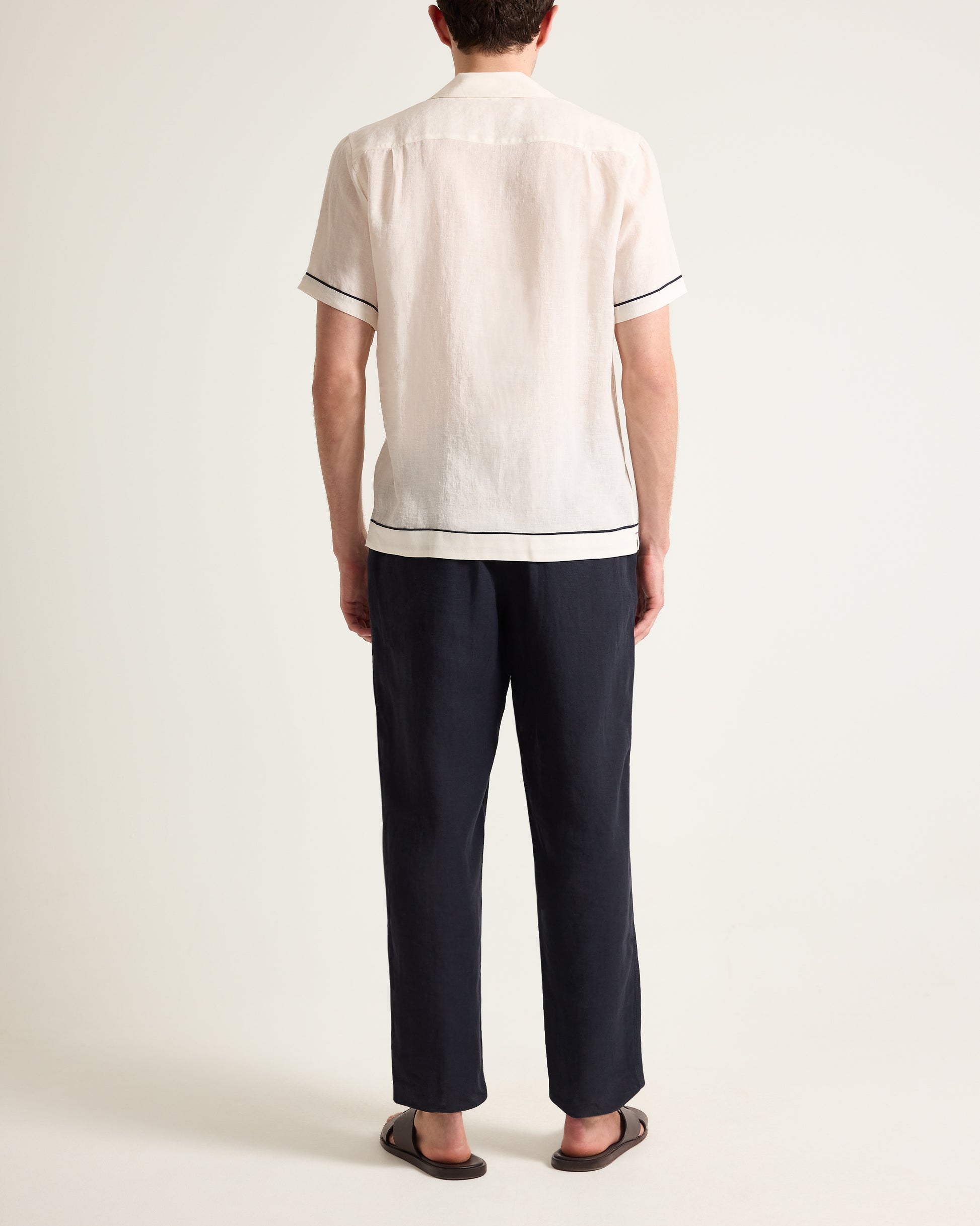 Person wearing a white shirt with black trim and dark pants on a plain background