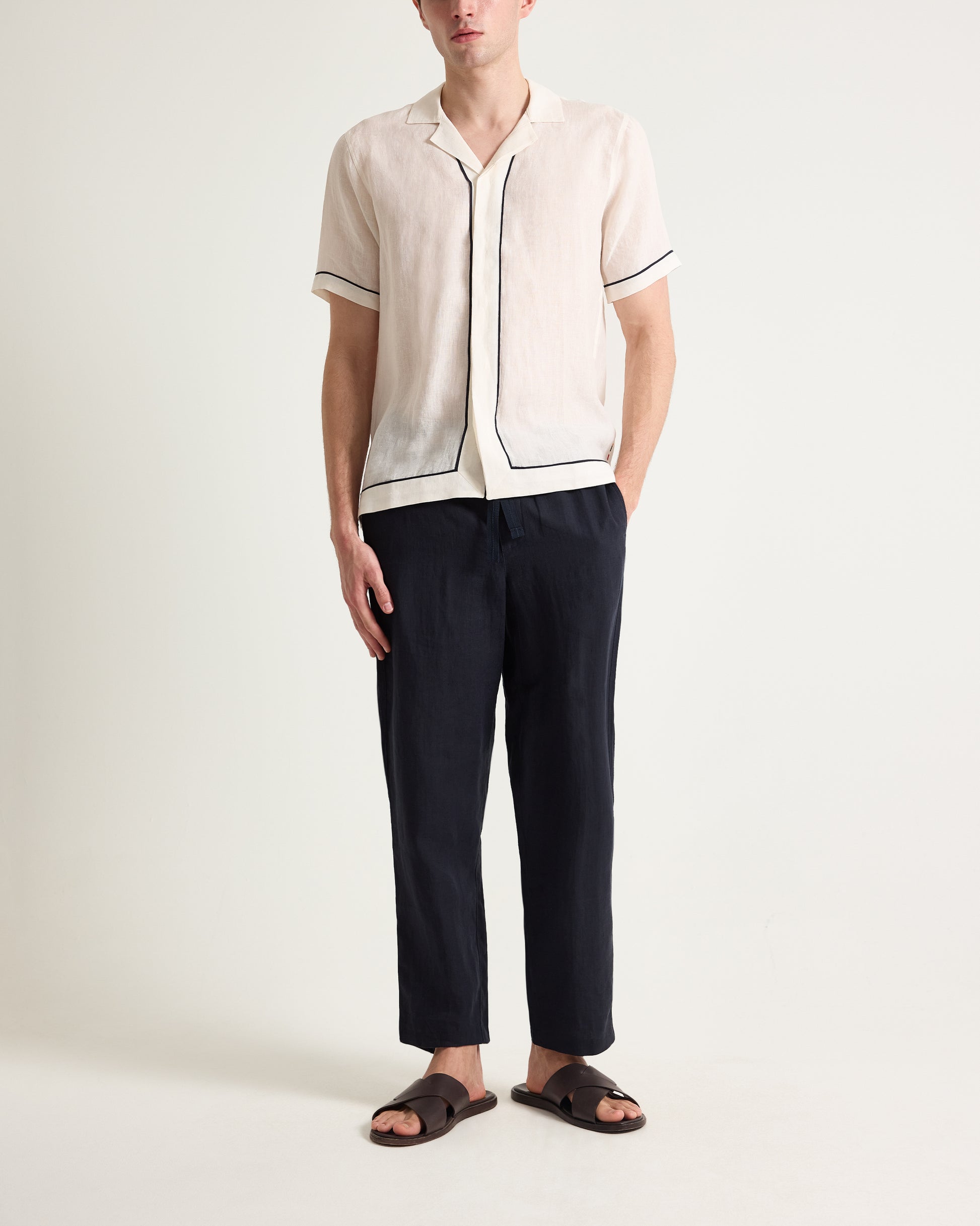 Person wearing a white shirt with black trim and dark pants on a white background