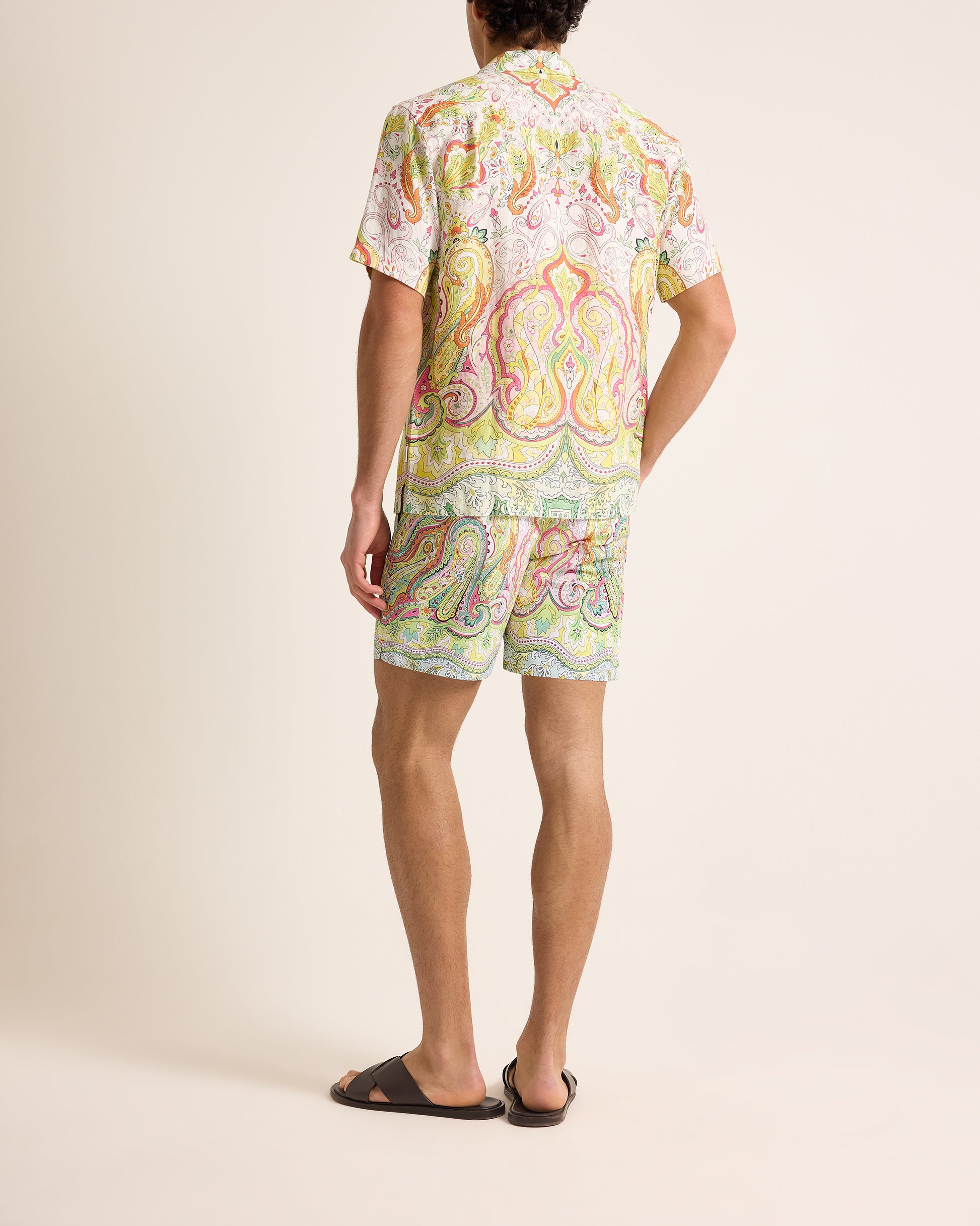 Person wearing a colorful paisley shirt and shorts set on a beige background