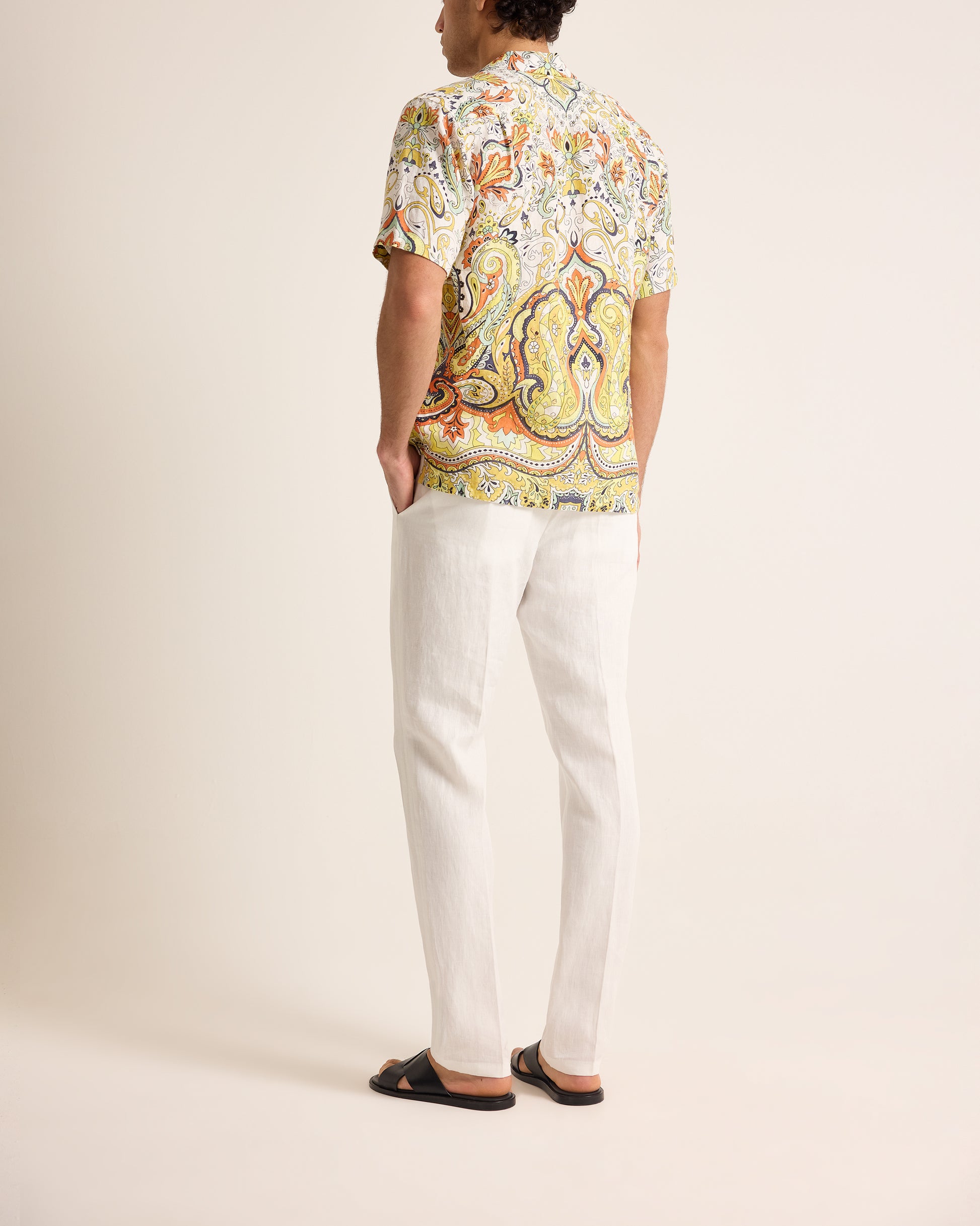 Person wearing a colorful patterned shirt and white pants on a plain background