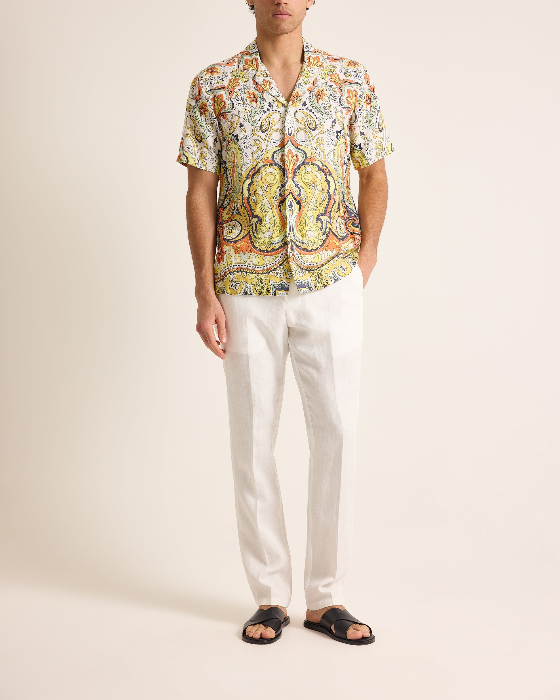 Man wearing a colorful patterned shirt and white pants on a plain background