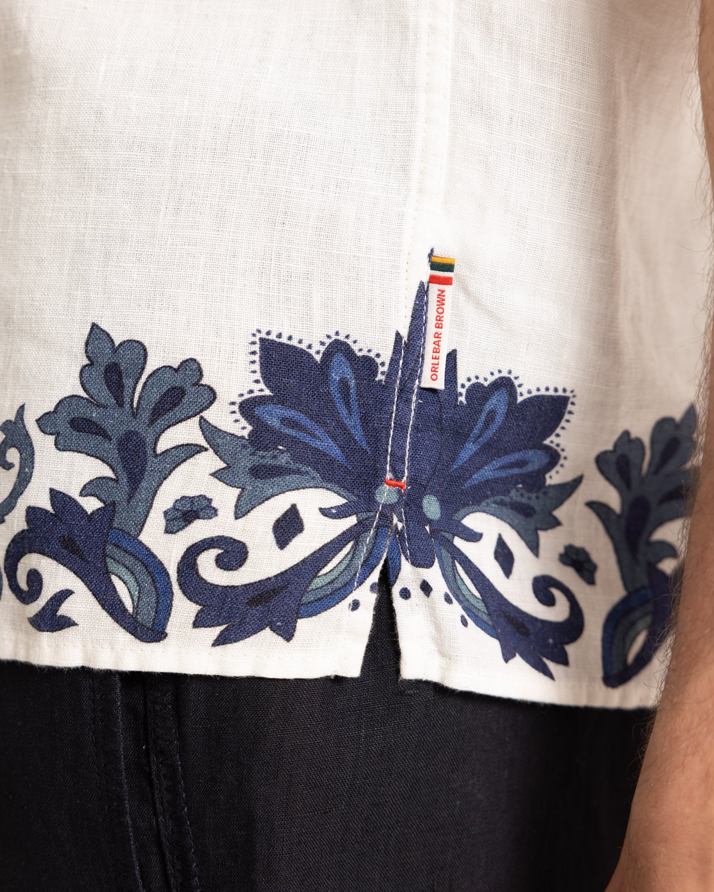Closeup of white linen shirt with blue printed border detailing and navy trousers