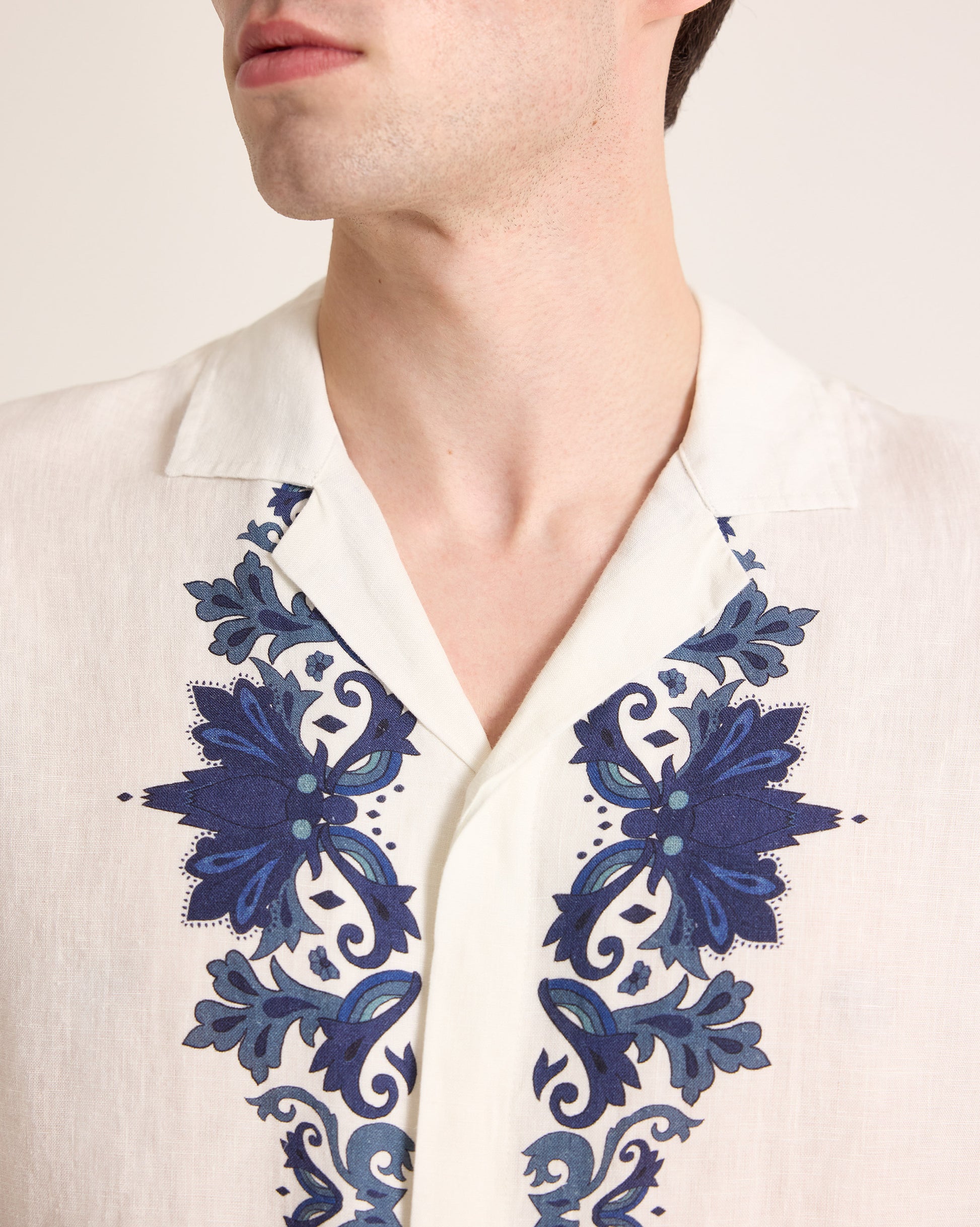 Close-up of a white shirt with blue floral embroidery on a plain background