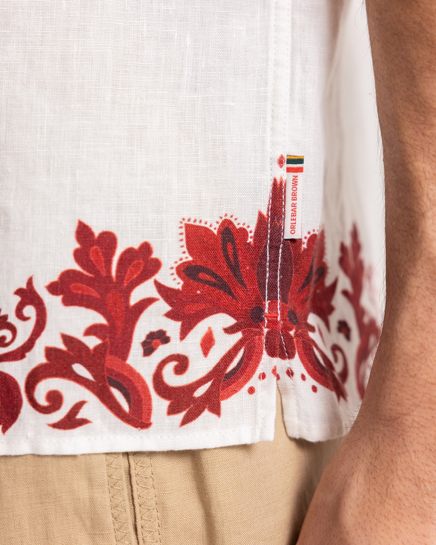 Closeup of white linen shirt with red printed border detailing and beige trousers