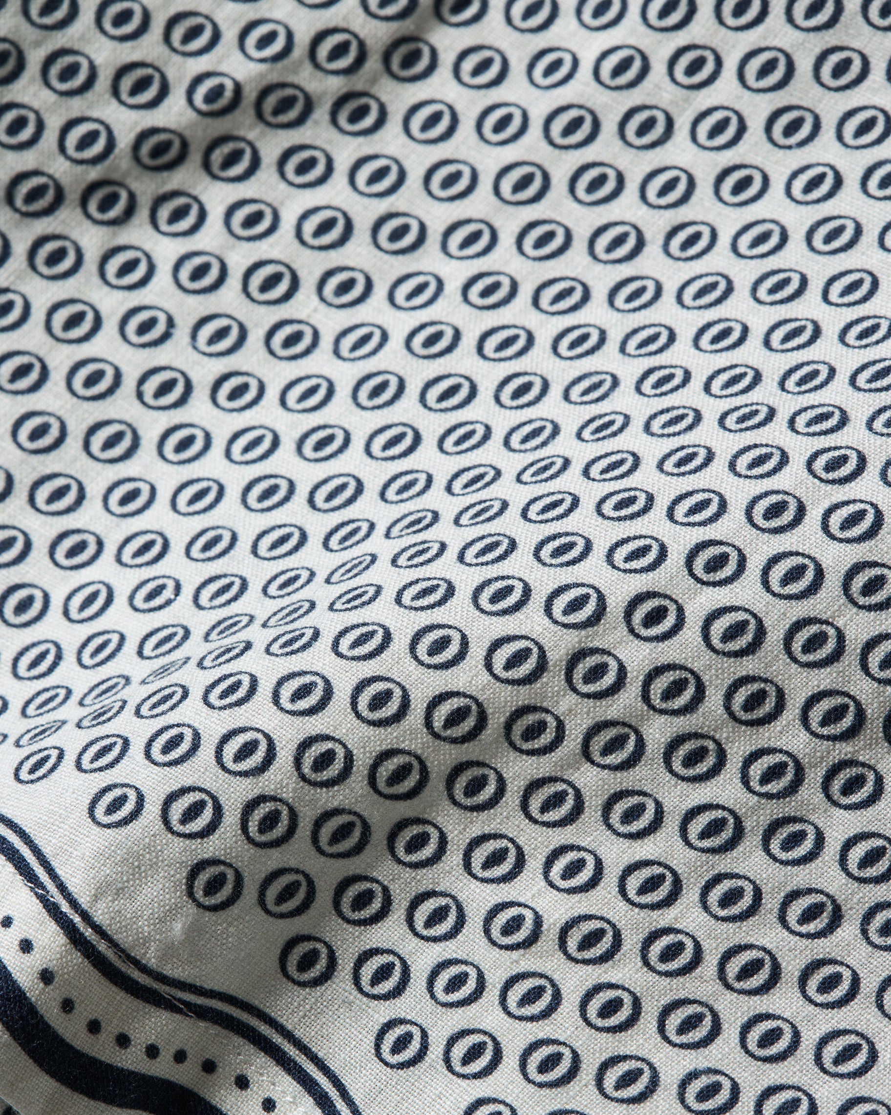 Close-up of a white fabric with a repeating navy blue circular dot pattern and a navy border along the bottom edge.