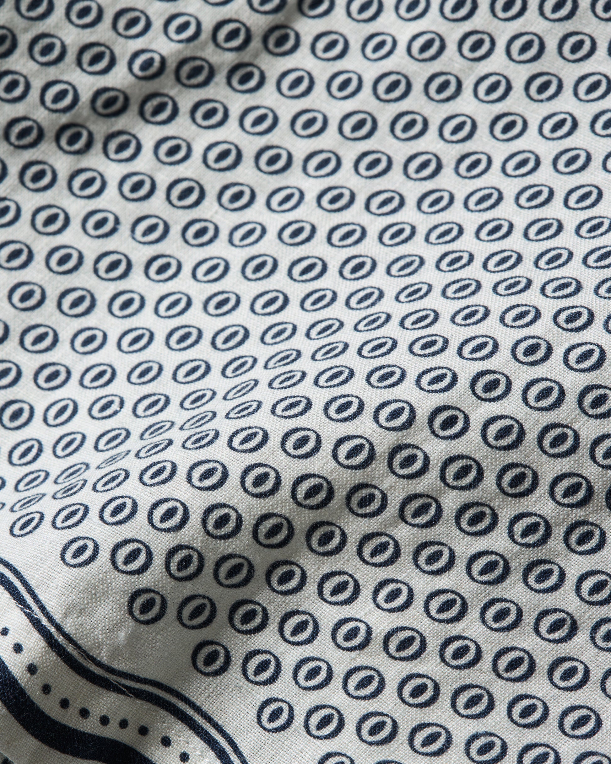 Close-up of a white fabric with a repeating navy blue circular dot pattern and a navy border along the bottom edge.