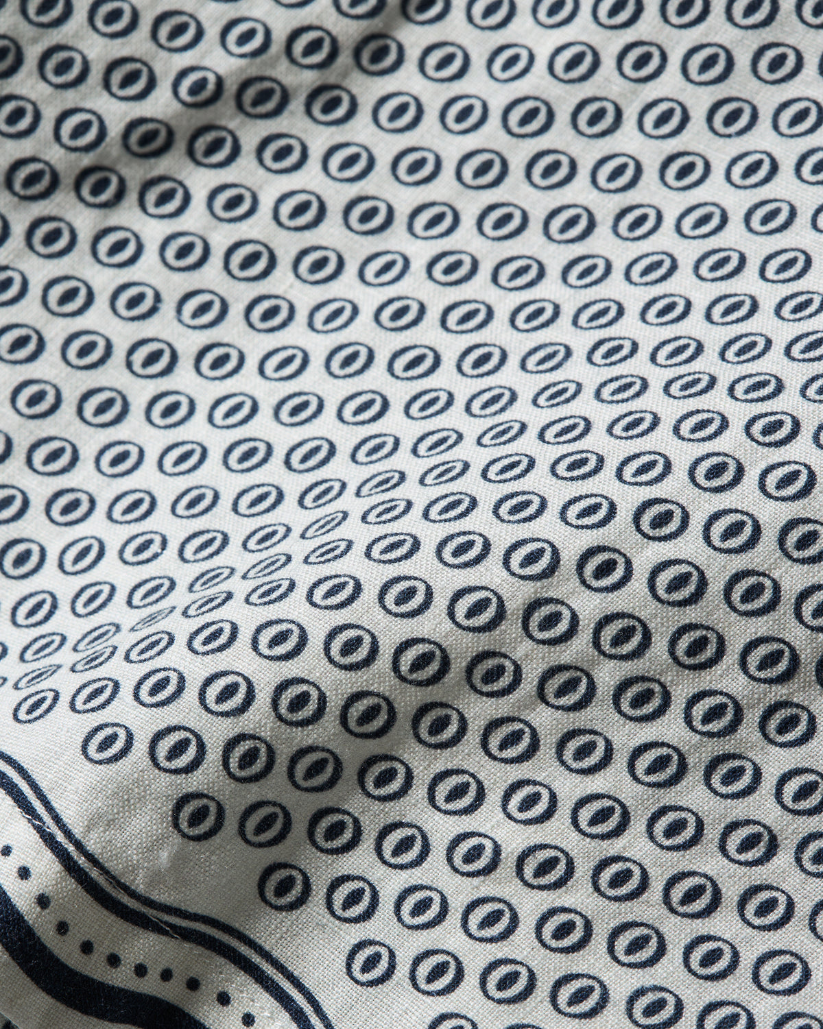 Close-up of a white fabric with a repeating navy blue circular dot pattern and a navy border along the bottom edge.