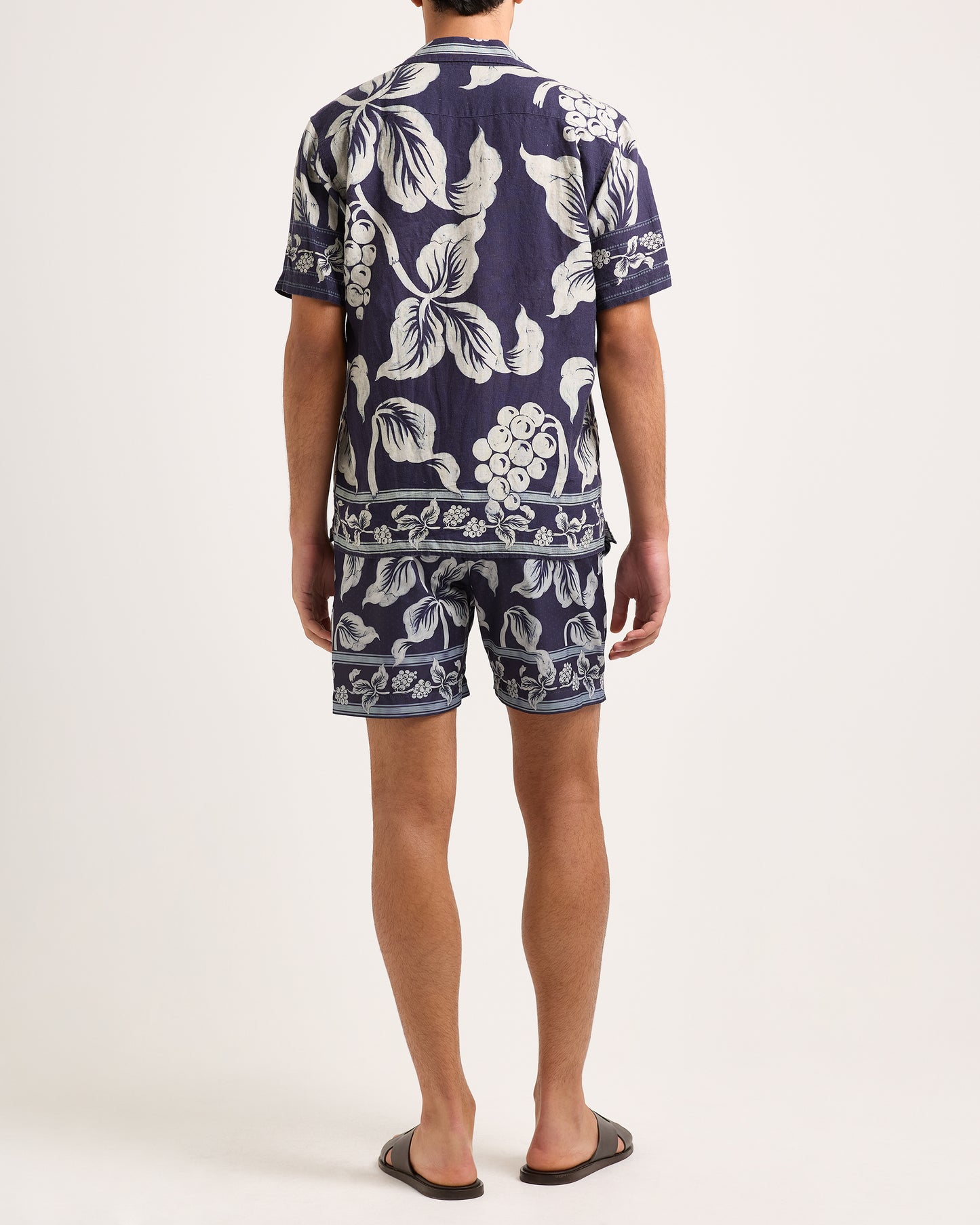 Man wearing a navy blue floral patterned shirt and shorts on a white background