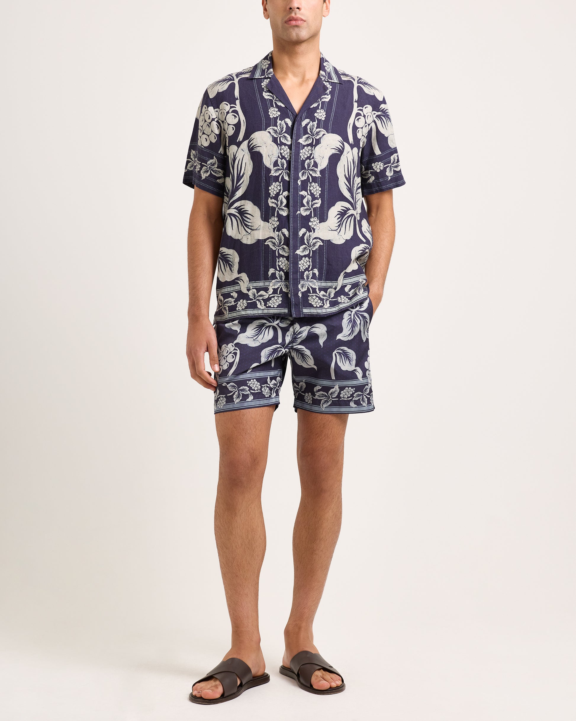 Man wearing a navy blue floral patterned shirt and shorts on a white background