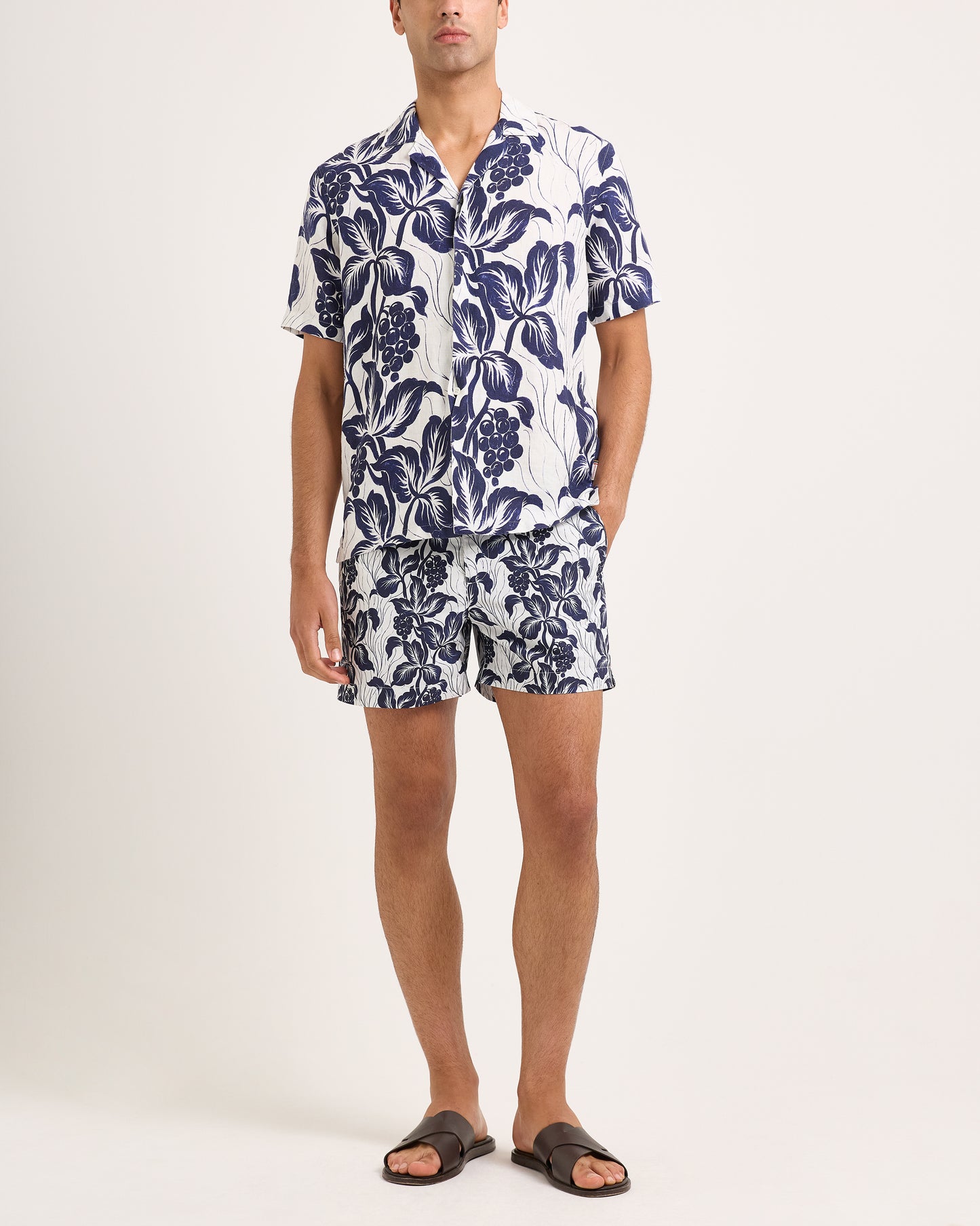Man wearing a navy floral shirt and shorts on a white background