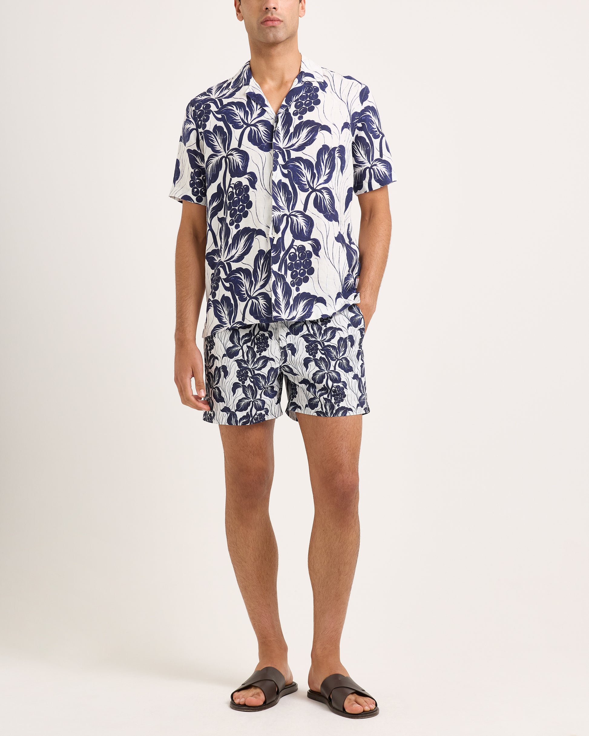 Man wearing a navy floral shirt and shorts on a white background