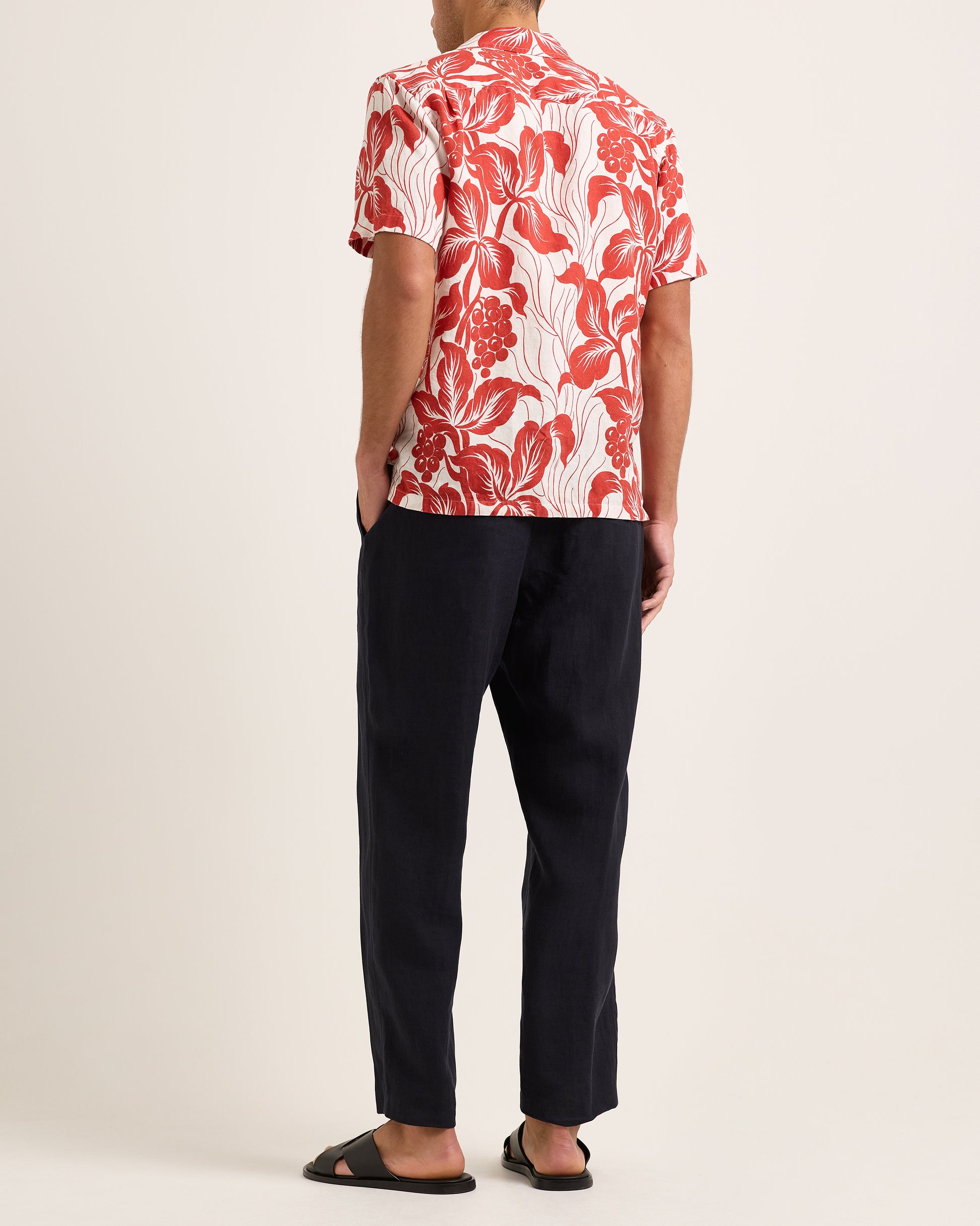 Person wearing a red and white floral shirt with black pants on a plain background