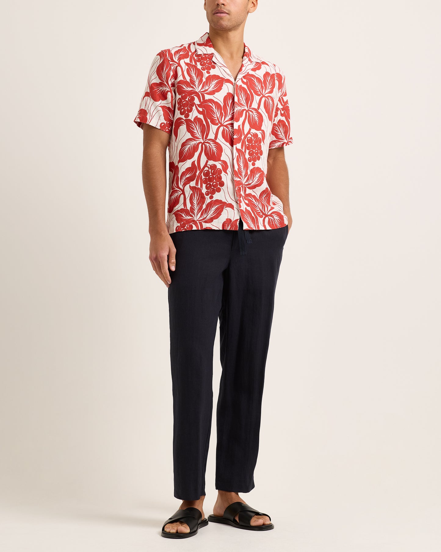 Person wearing a red and white floral shirt with black pants on a plain background