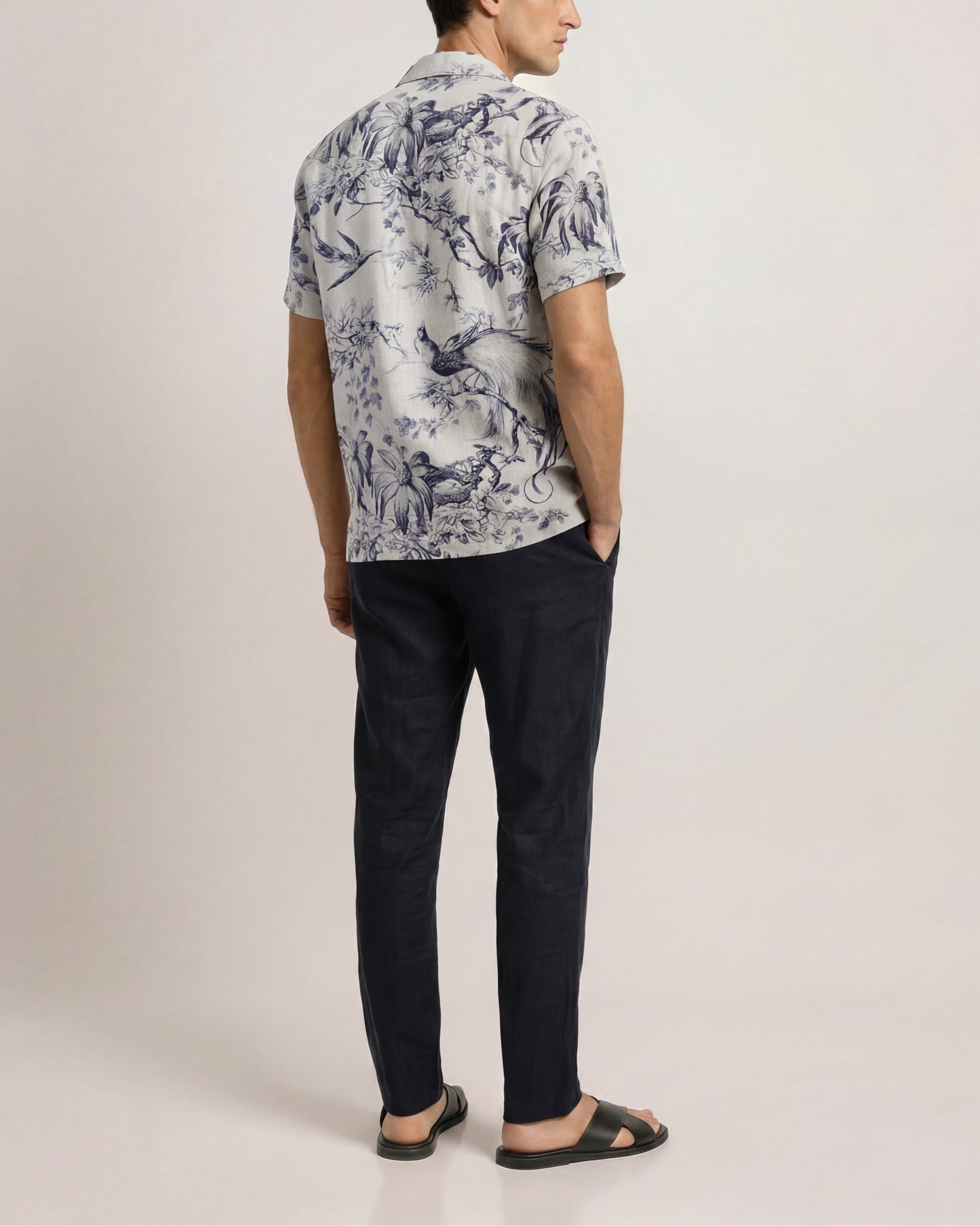 Man wearing a patterned shirt and black pants on a plain background