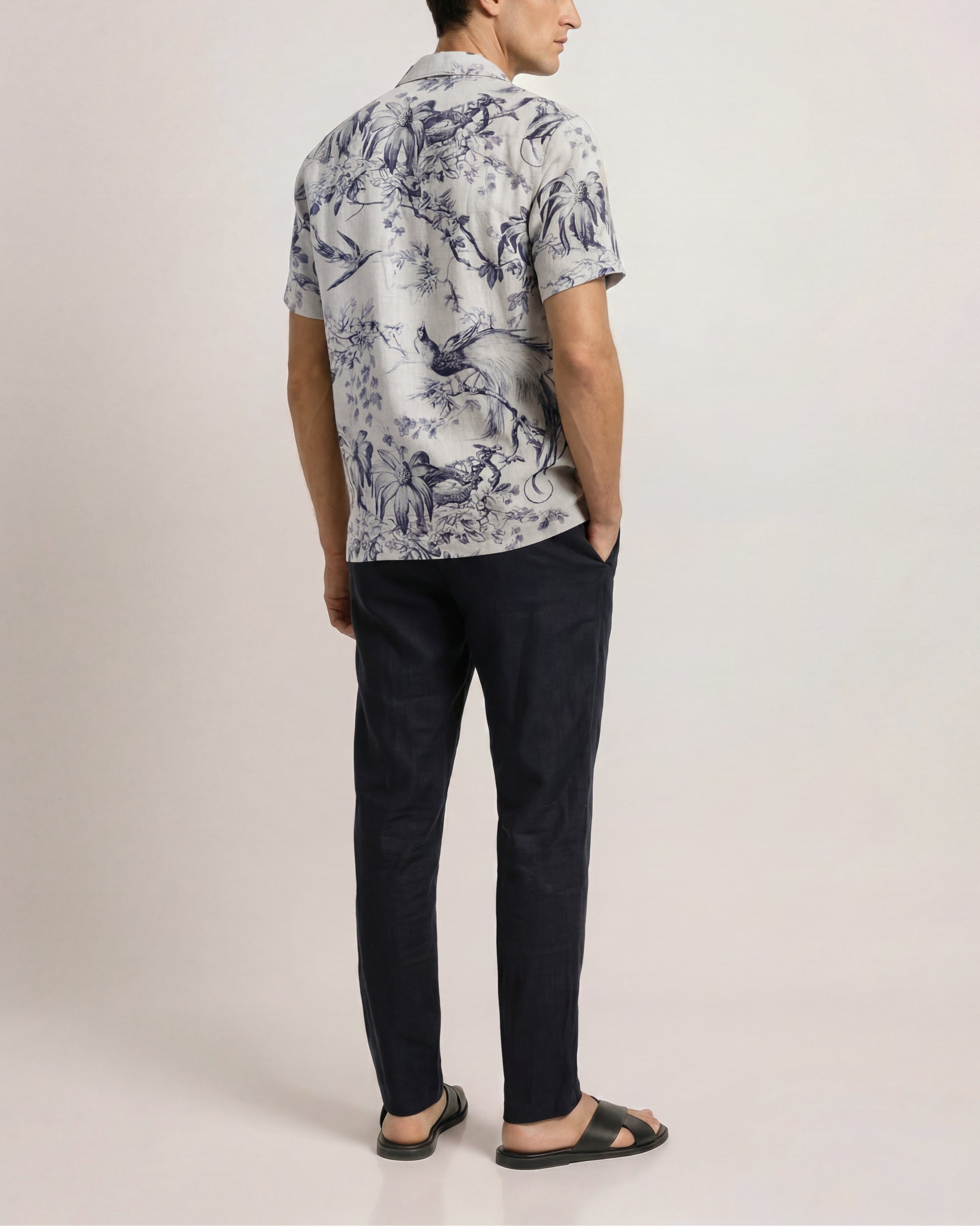 Man wearing a patterned shirt and black pants on a plain background