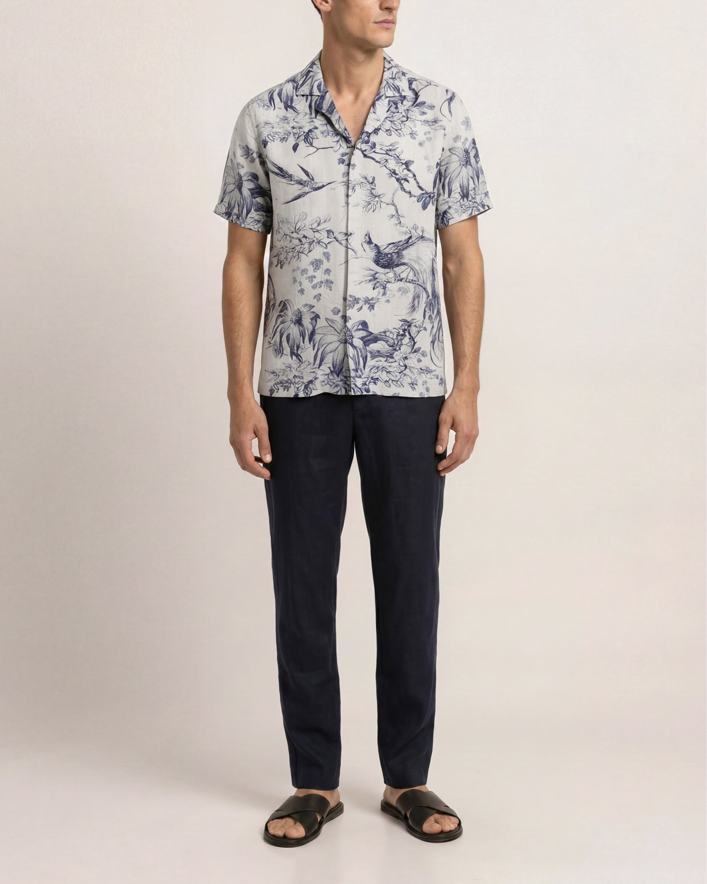Man wearing a patterned shirt and dark pants on a plain background