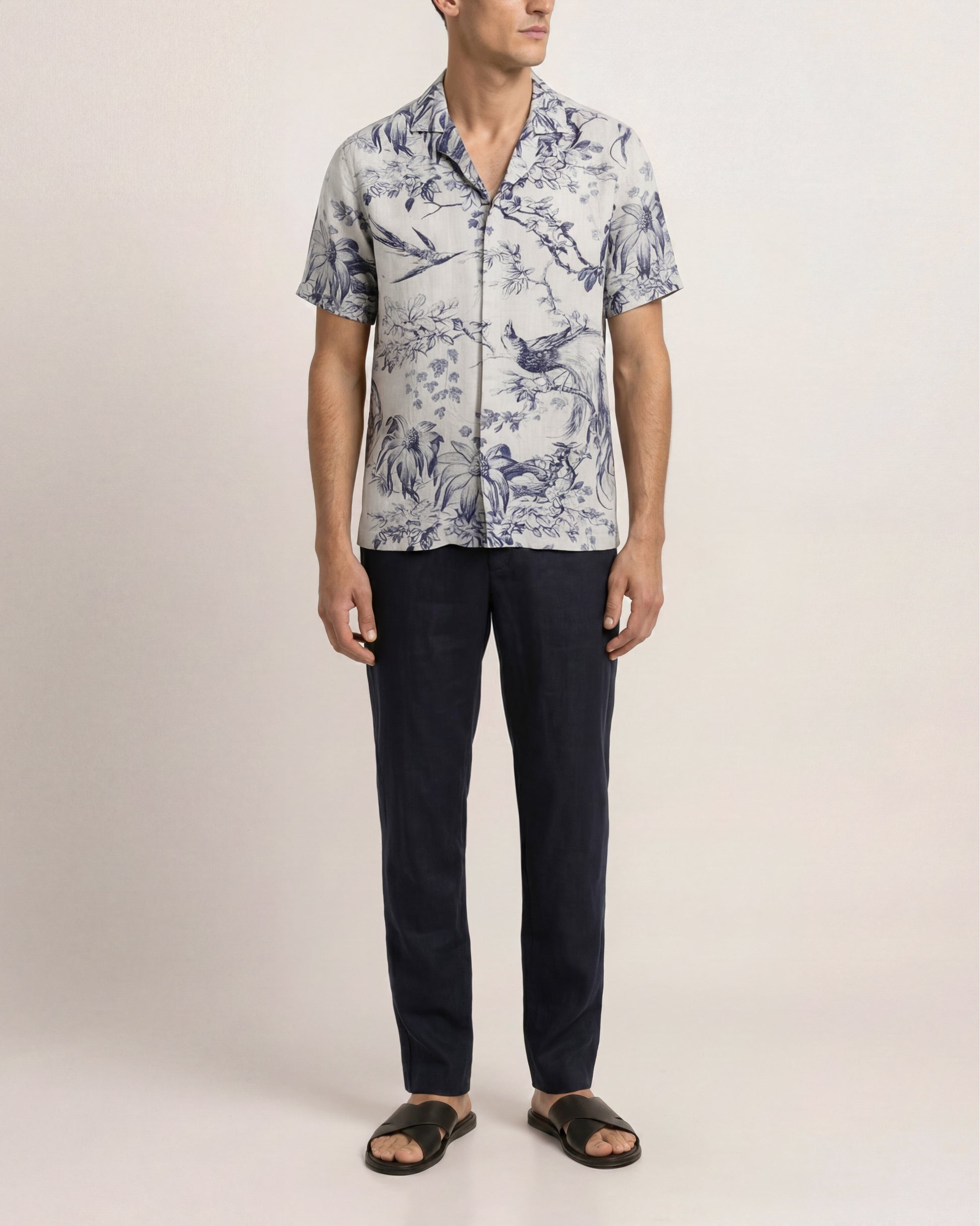 Man wearing a patterned shirt and dark pants on a plain background