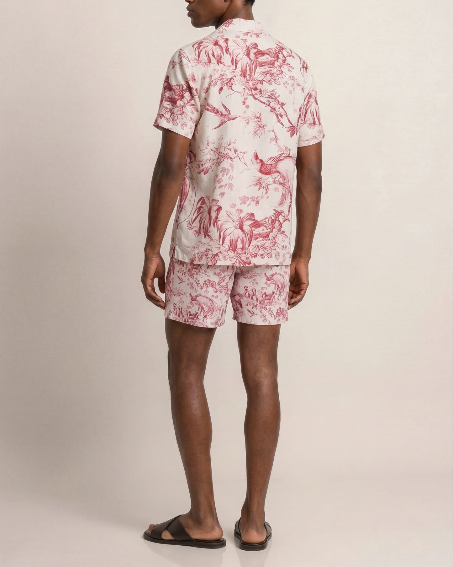 Person wearing a red and white floral shirt and shorts set on a beige background