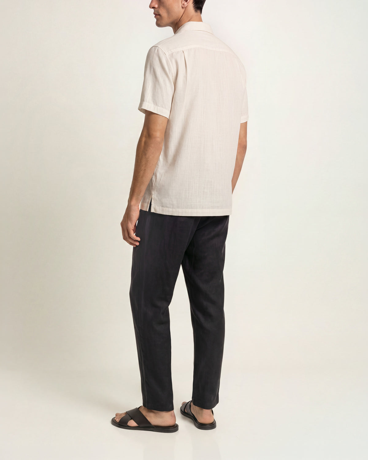 Man wearing white short sleeve shirt with black trousers and brown sandals on a plain background
