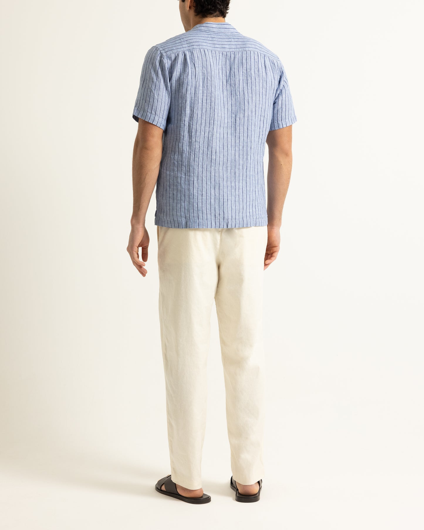Man wearing blue short sleeve striped shirt with light beige trousers on a plain background