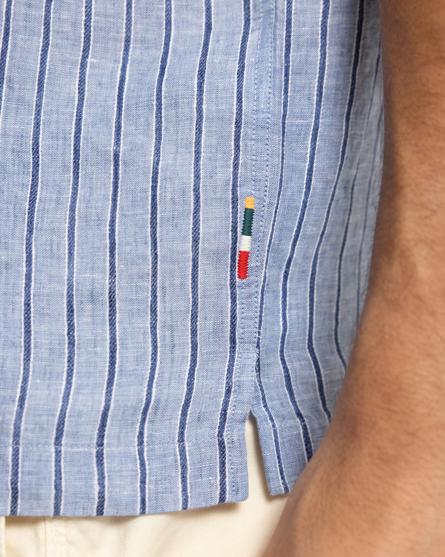 Close-up of a blue striped shirt with a small logo on a person's arm.