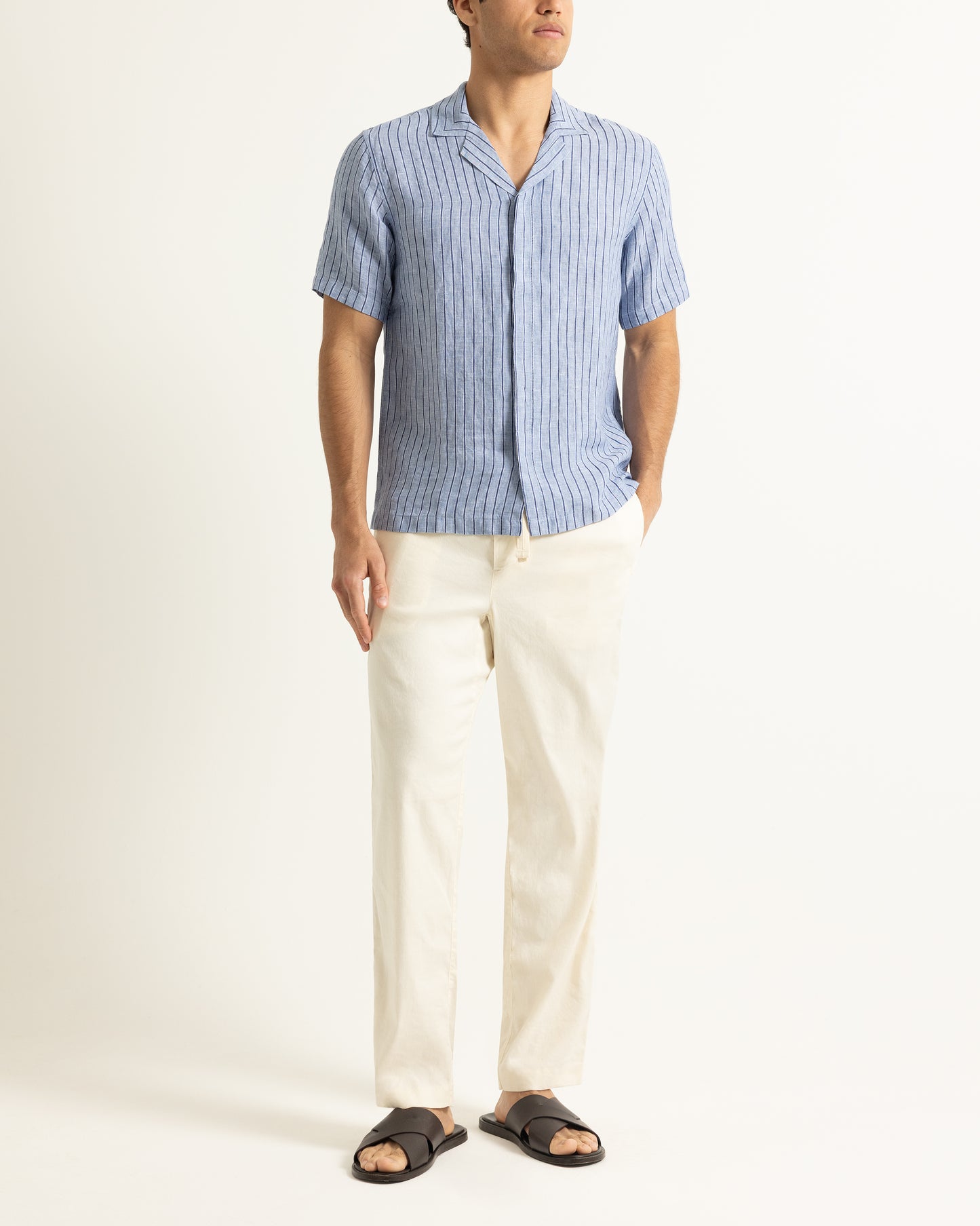Man wearing blue short sleeve striped shirt with light beige trousers on a plain background